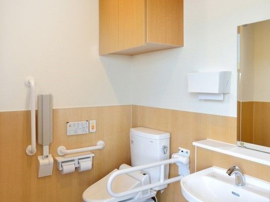 両側に手すりが取り付けてある収納付きトイレの様子。洗面台には鏡もついている。