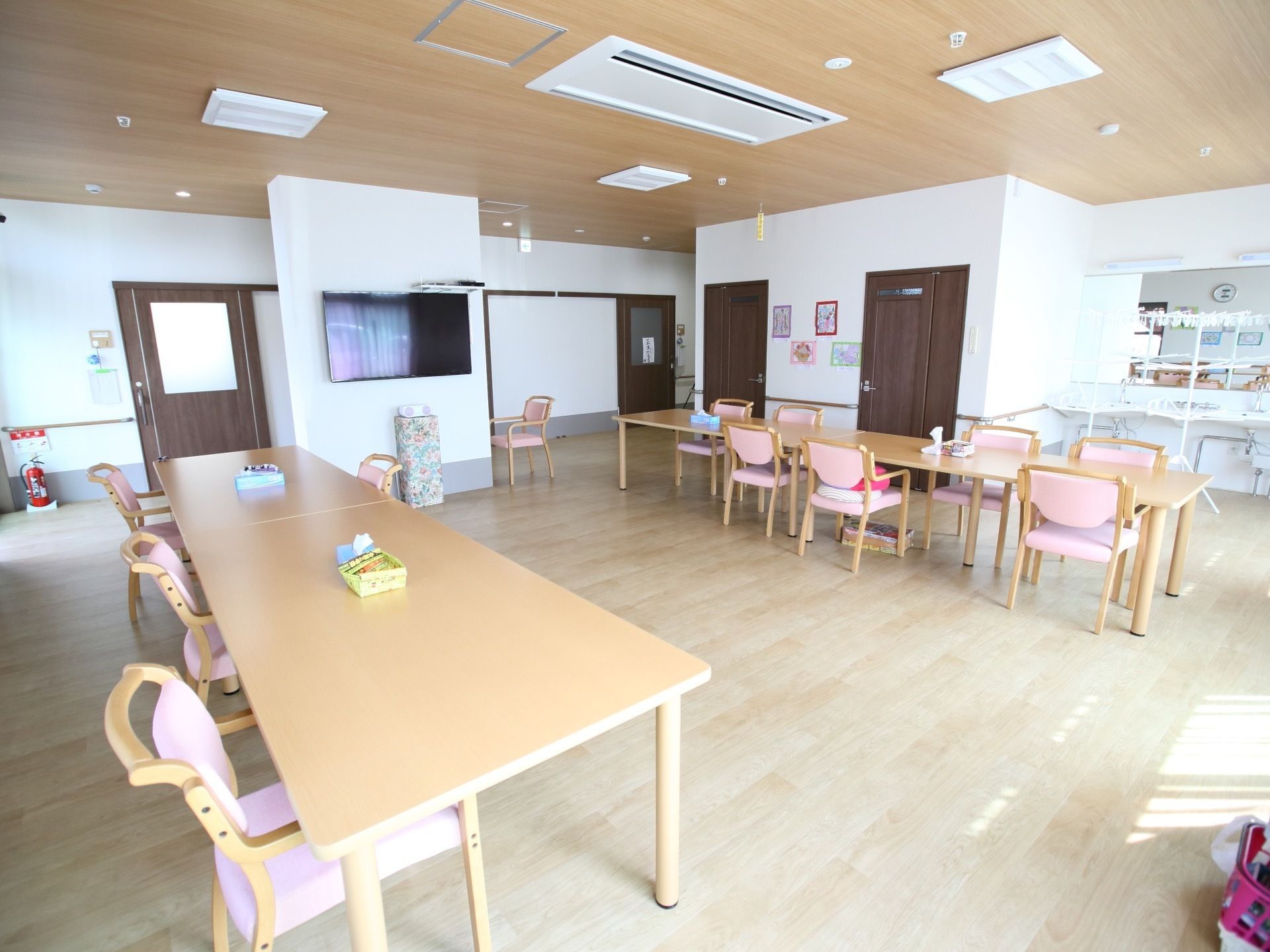 広々としたフローリングの部屋にテーブルセットが並べられている。天井も木目調で温かみがあり、空調が設置されている。