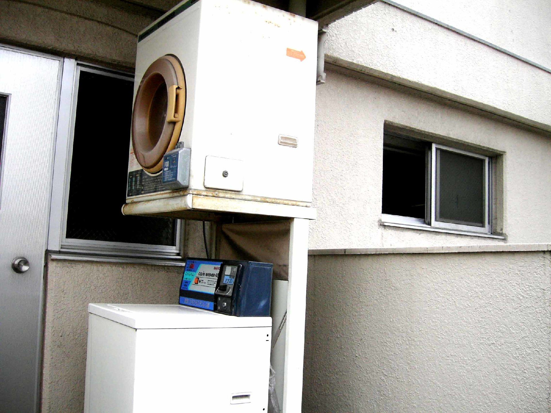 コイン式の洗濯機の上に乾燥機が設置されている。壁には二つ窓があり、窓の外は夜のように暗い。