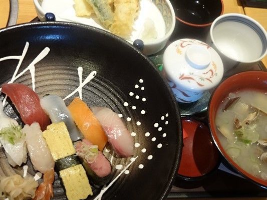 黒い皿の上に載っている握りずし、茶わん蒸し、お吸い物、天ぷらなどが写っている