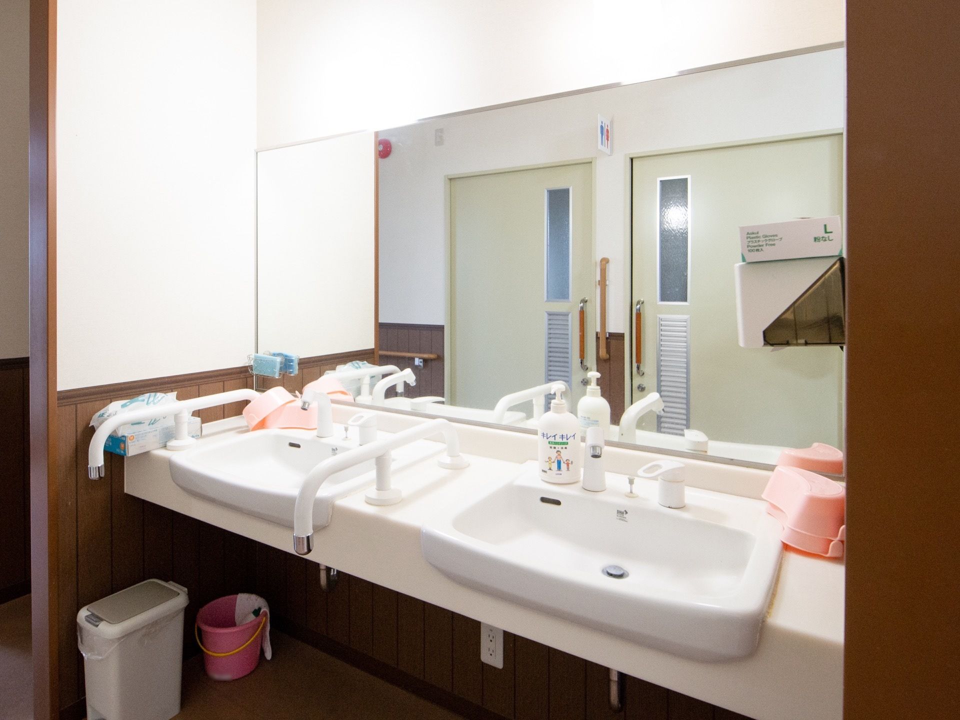 共有トイレと廊下を挟んで向かい側に洗面台が２台設置されている。利用しやすいように照明で明るく照らされている。