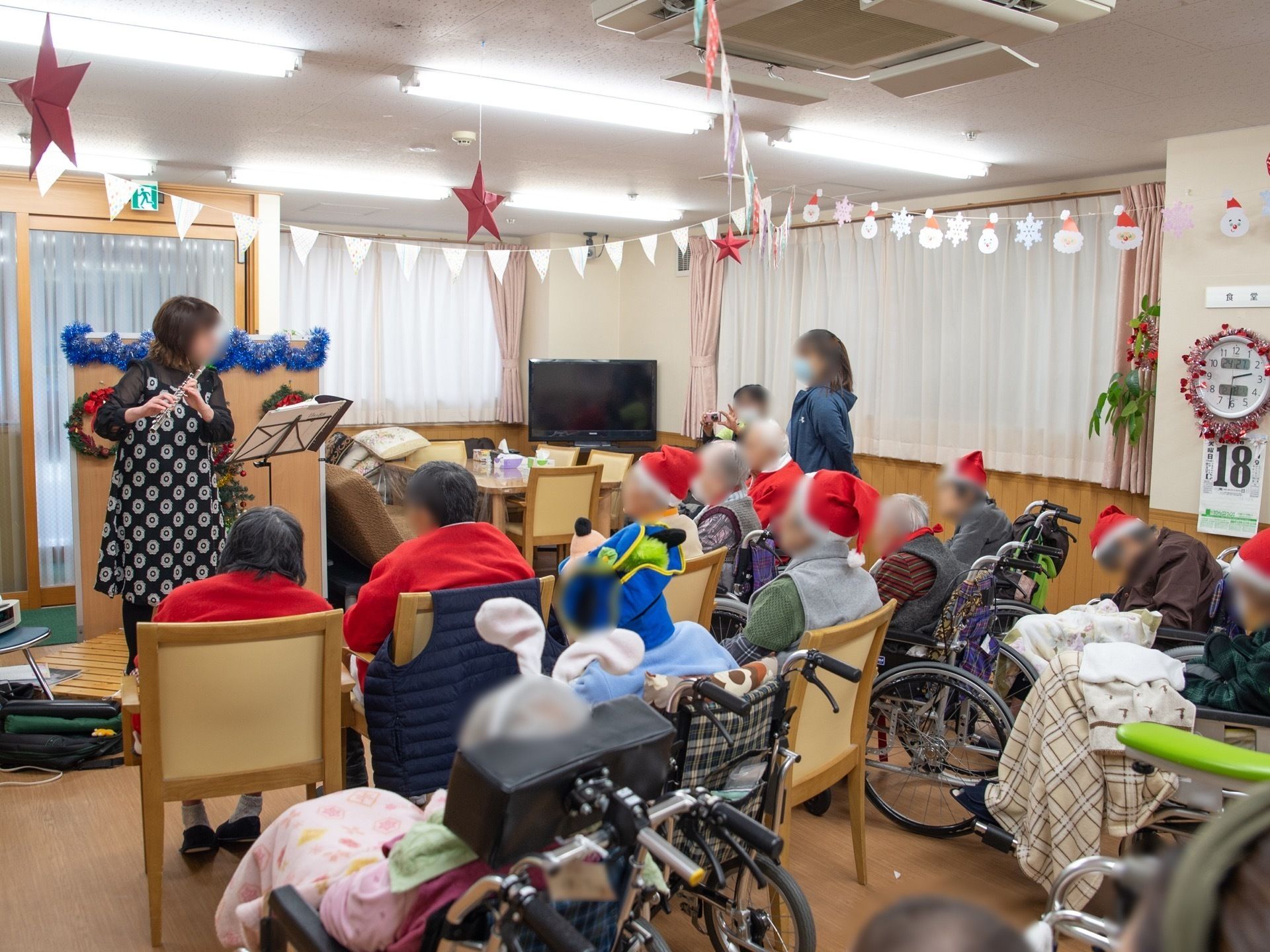 フルートを吹いている女性演奏者を見ている多くの入居者様