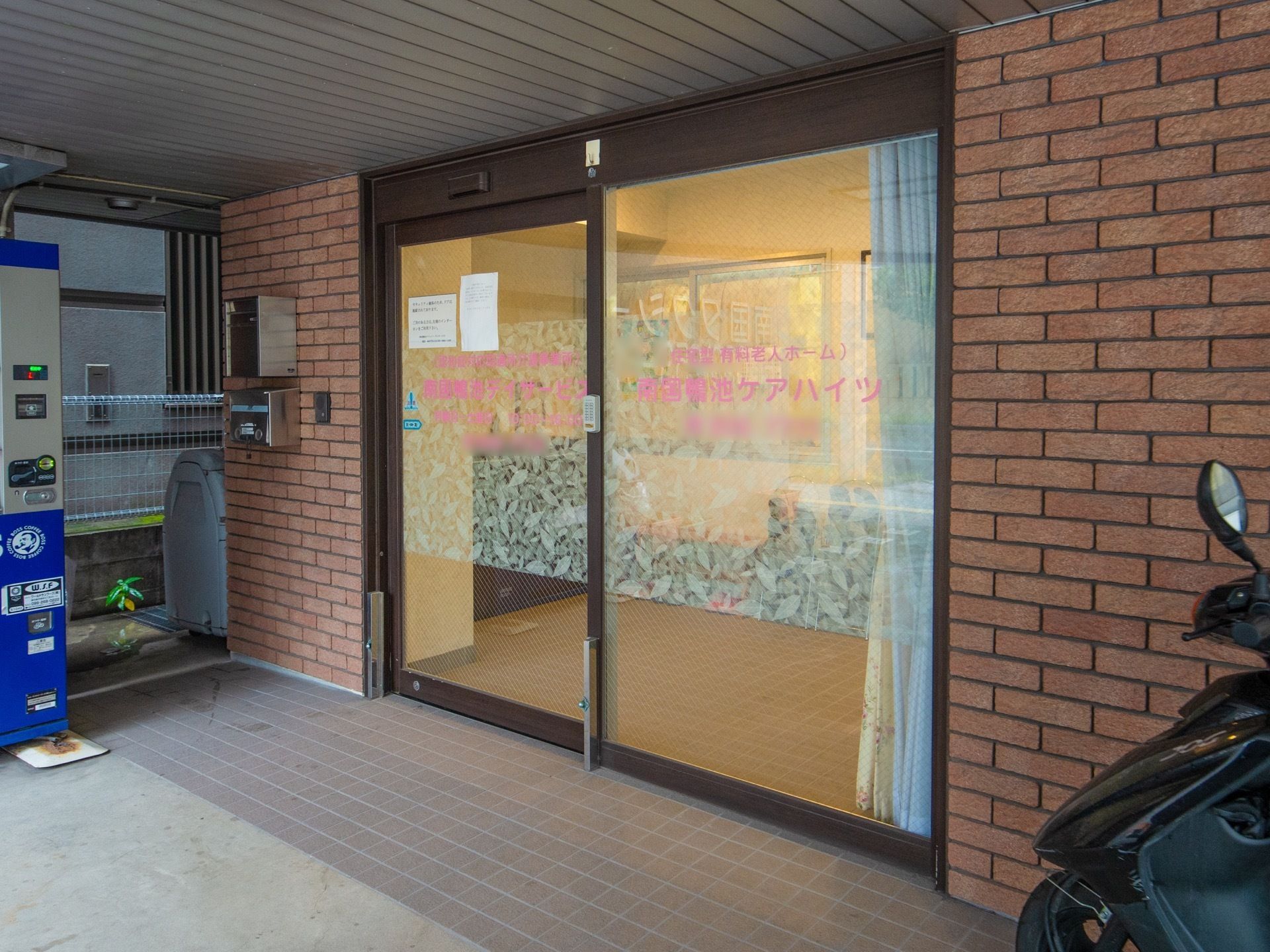 入口は自動ドアになっている。ドアの左横にはインターホンとポストがあり、玄関前には自動販売機が設置されている。