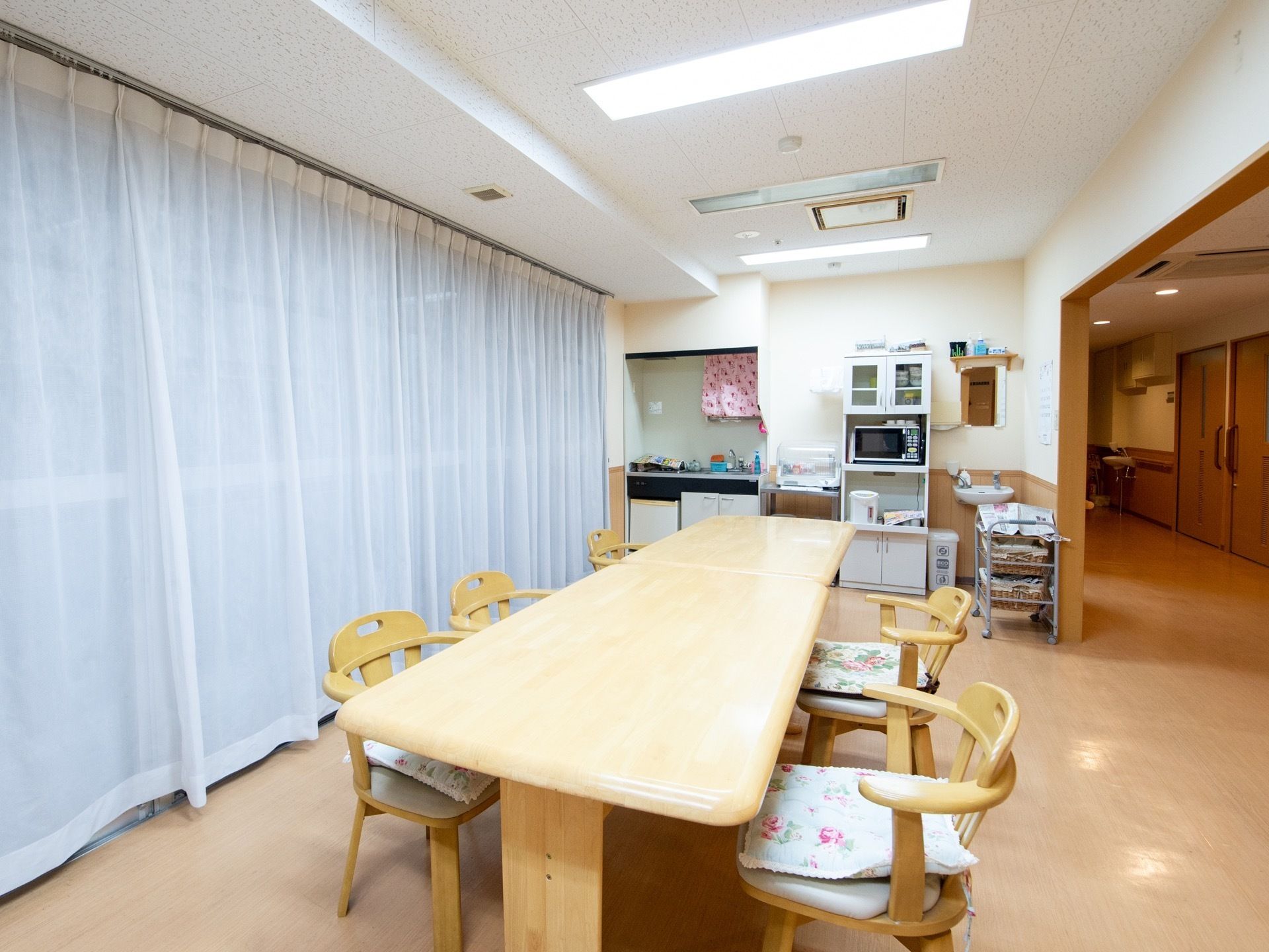 廊下から直結している食堂には、長い食卓と肘掛け付きの椅子が並んでいる。奥には小さなキッチンと手洗い場、電子レンジなどの家電が置かれている。