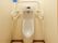 トイレ内に手をかざして水洗するタイプの男性用小便器がある。便器の上部と左右には、白い手すりがついている。