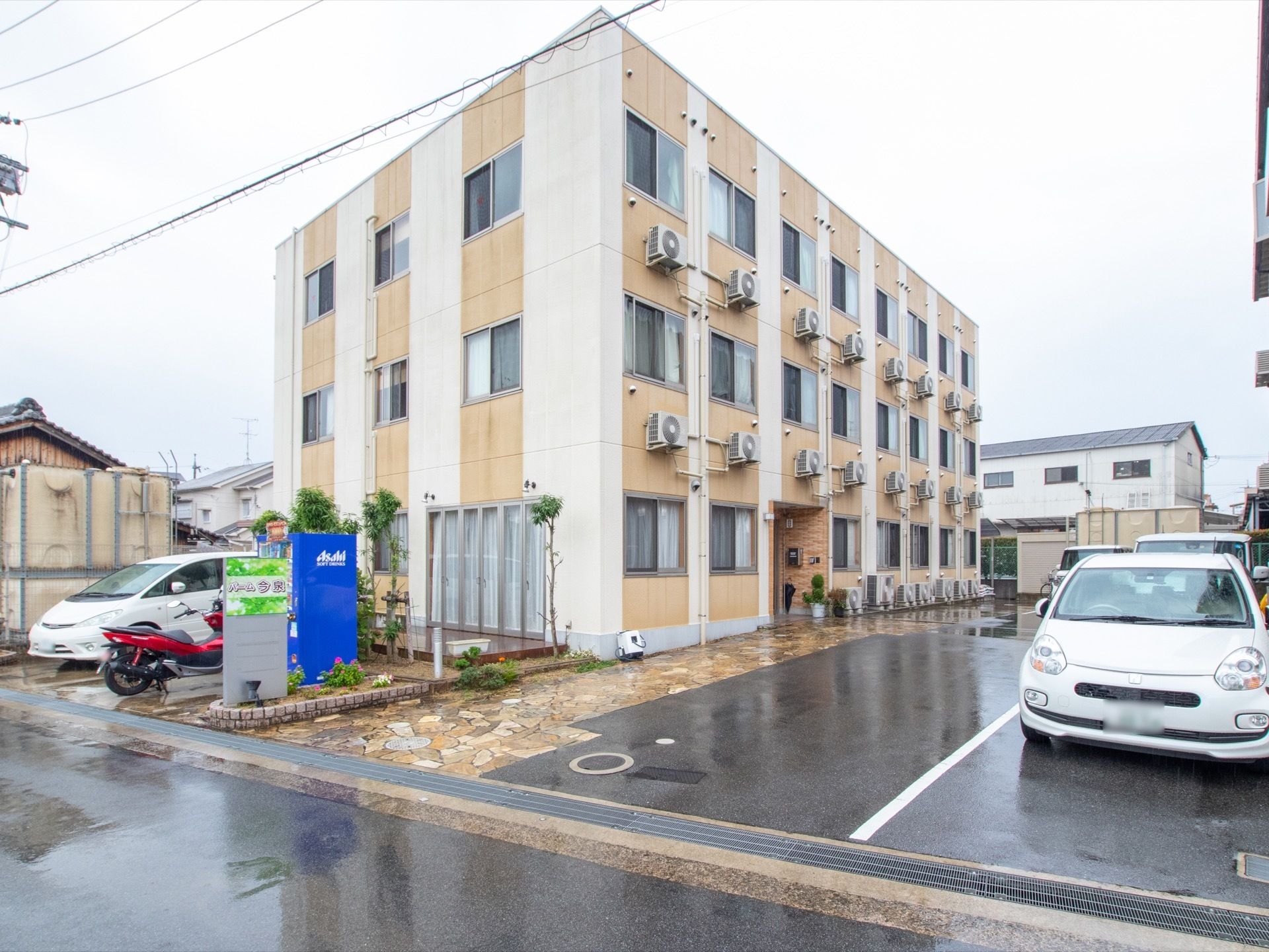 イエローベースの3階建ての施設建物である。各部屋には、エアコン室外機が設置されている。石畳の通路が建物に沿って続いている。