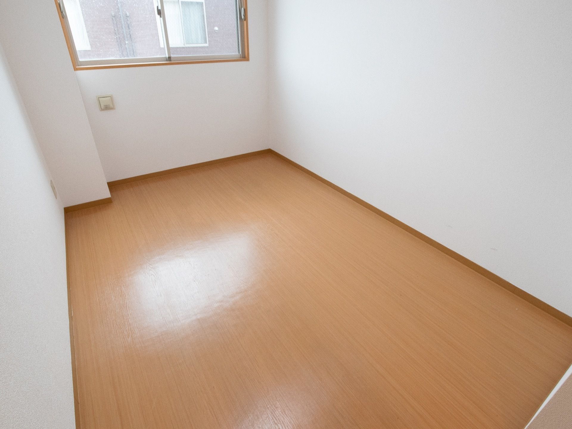 真っ白な壁と木目調のフローリングの床になっている居室である。部屋の窓からは、隣にある新館の建物が見えている。