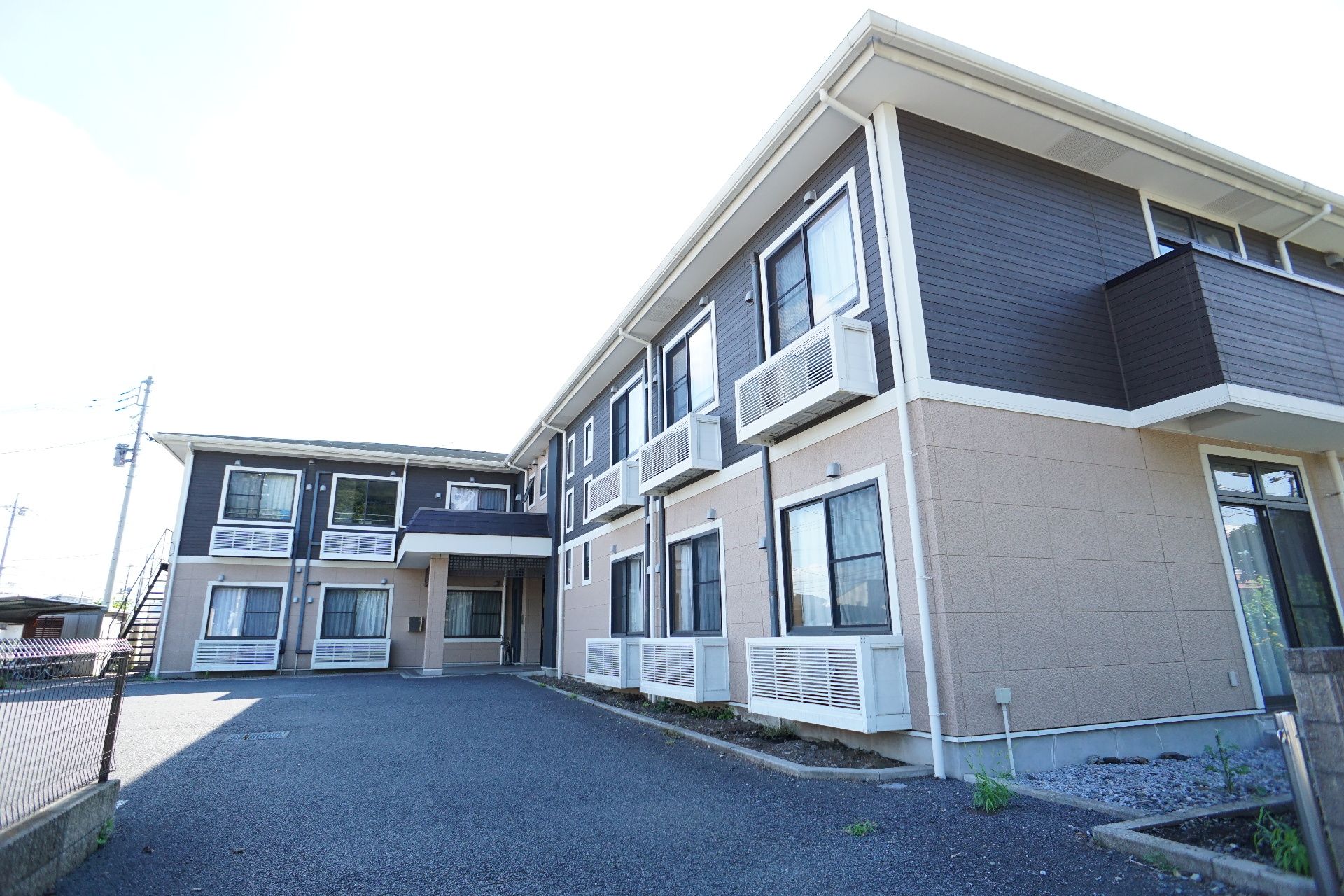 黒とベージュの外観でL字に曲がった２階建ての建物