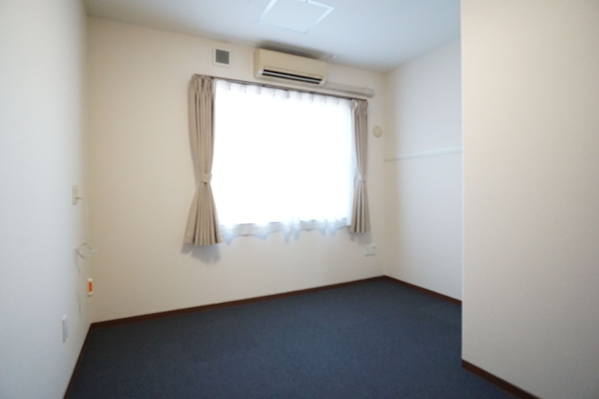 カーテンのついた窓がある何も置かれていない白い壁の部屋