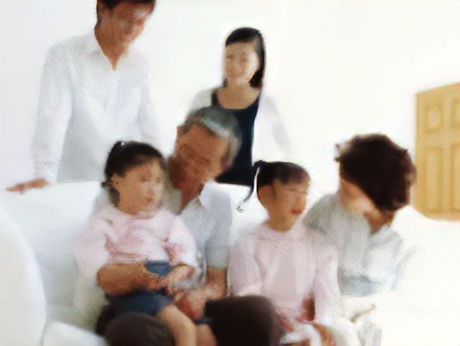 白いソファに座った高齢の夫婦がピンクの服を着た孫娘2人と笑顔で会話。ソファの後ろでは子供たちの親が笑顔で見守っている。