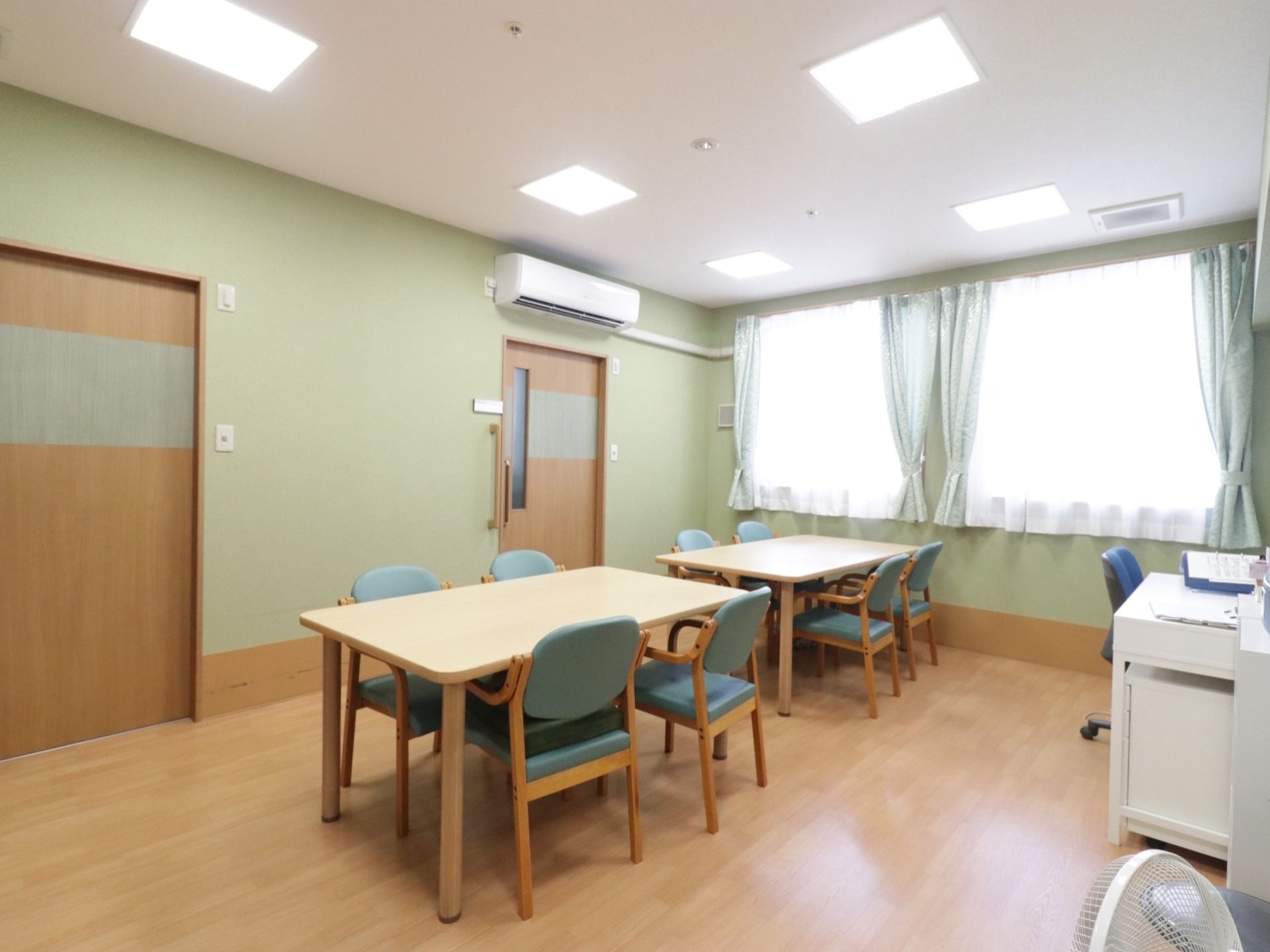 リビングには4人掛けのダイニングセットが2つ並んでいる。壁一面が窓になっていて、明るい空間だ。エアコンも完備されている。