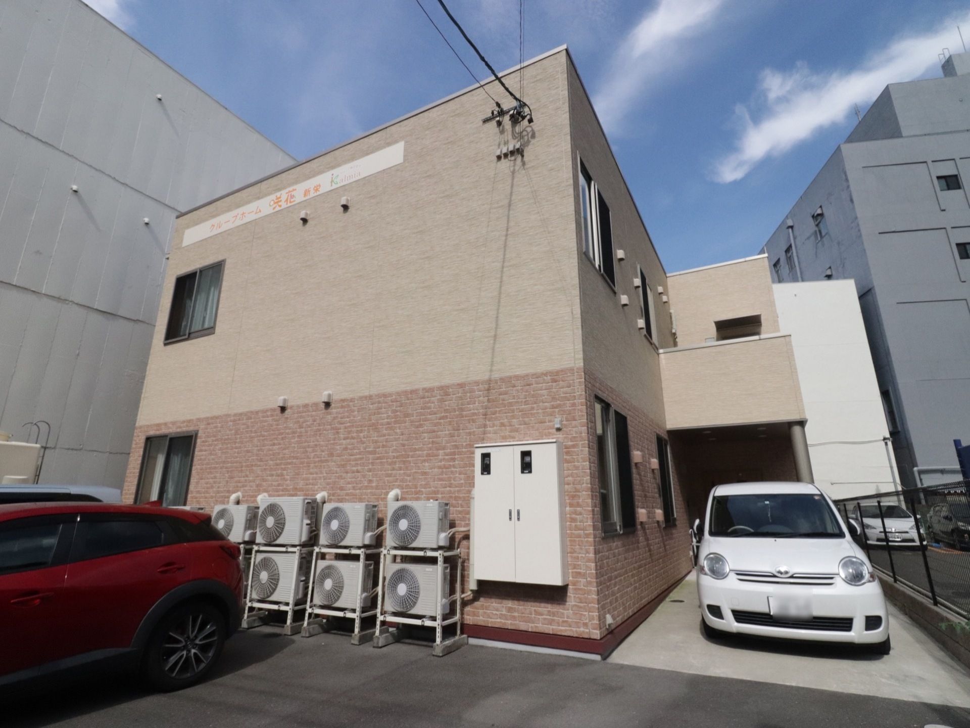 施設は茶系のスタイリッシュなデザインの建物で、一見グループホームには見えない。外壁の上部分に施設名の入った白い看板がある。