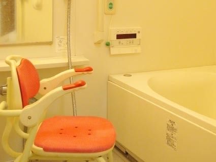 医療スタッフに車いすを押されて微笑んでいる。外に出て空気を感じている高齢者がひとり。リラックスしているので表情が柔らかい