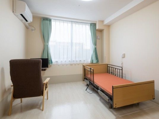 エアコン付き・窓付きの小さな部屋。ベッドと椅子、調度品が置かれているのが分かる