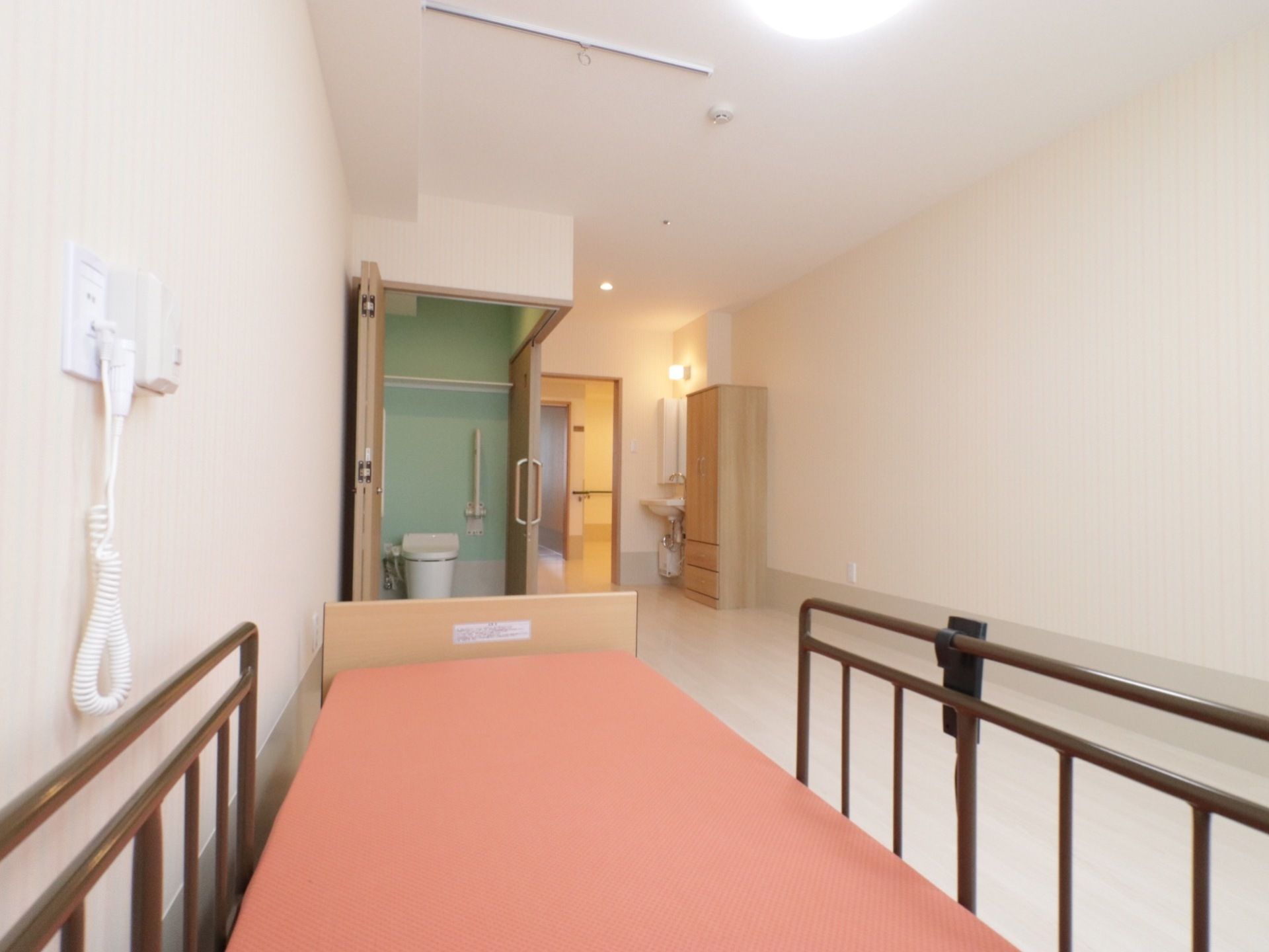 居室にはトイレと洗面台、大きな洋服ダンスが入口の周囲に設置されている。居住スペースには介護用ベッドが置かれている。