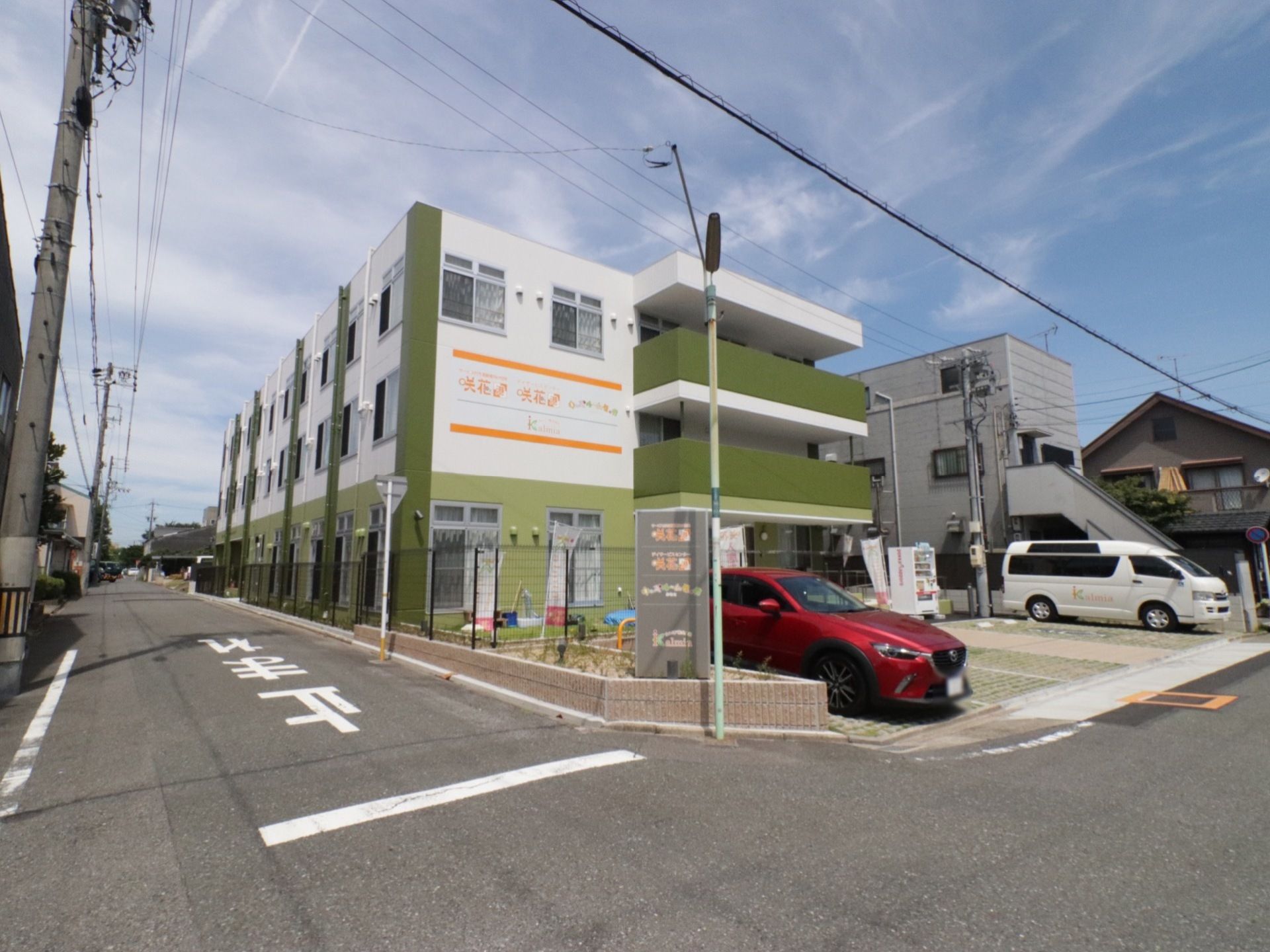 施設の外観は、白と緑の配色である。入口の前には、車を数台置くことができる駐車場スペースが確保されている。