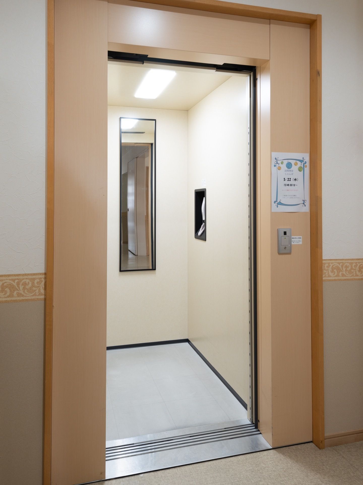 廊下の一角にエレベーターのドアがある。エレベーター内部は明るく、奧の壁には縦長の鏡が設置されている。