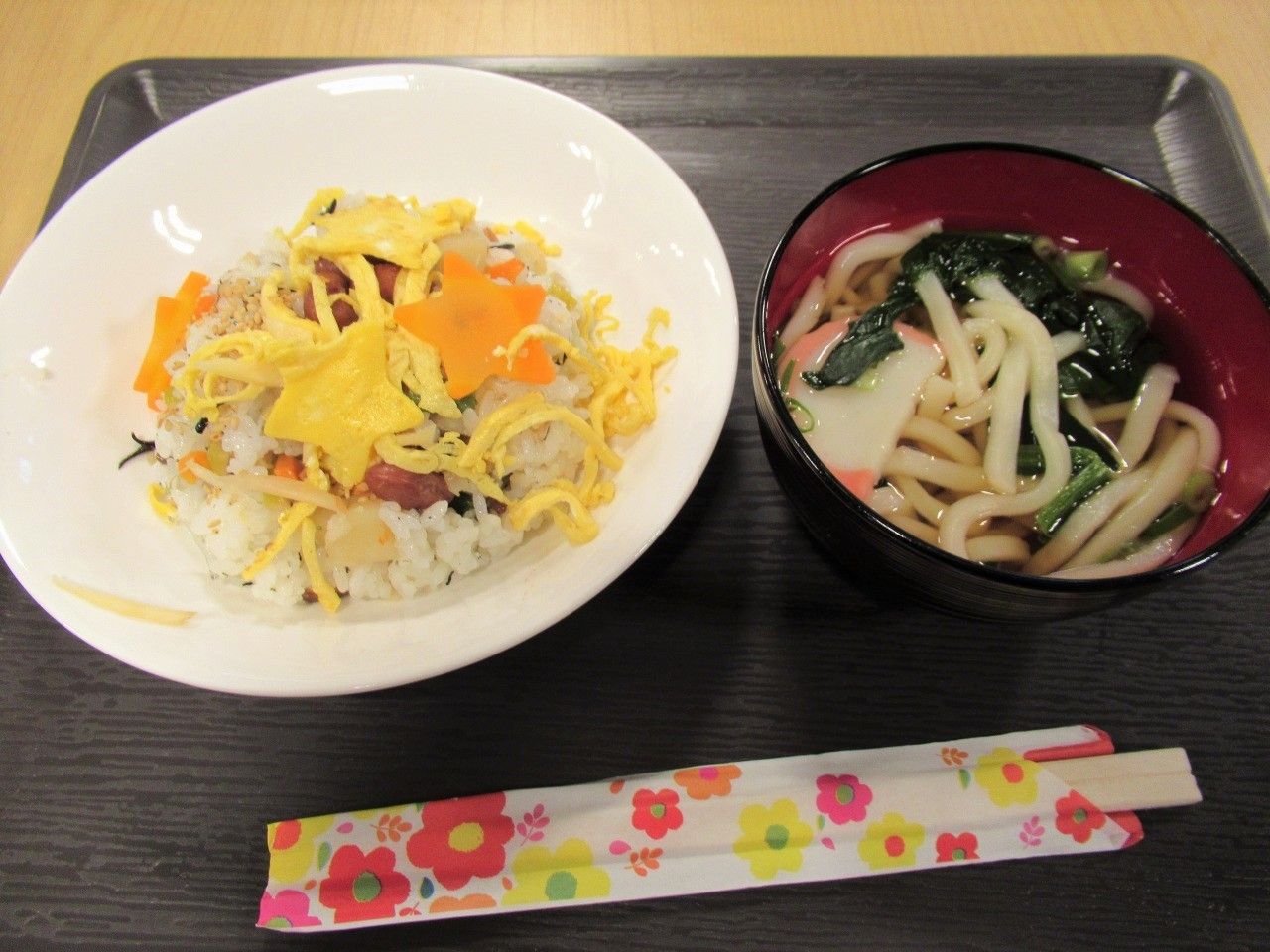 黒いお盆に星型の人参と卵が乗ったちらし寿司とうどんが乗っている。