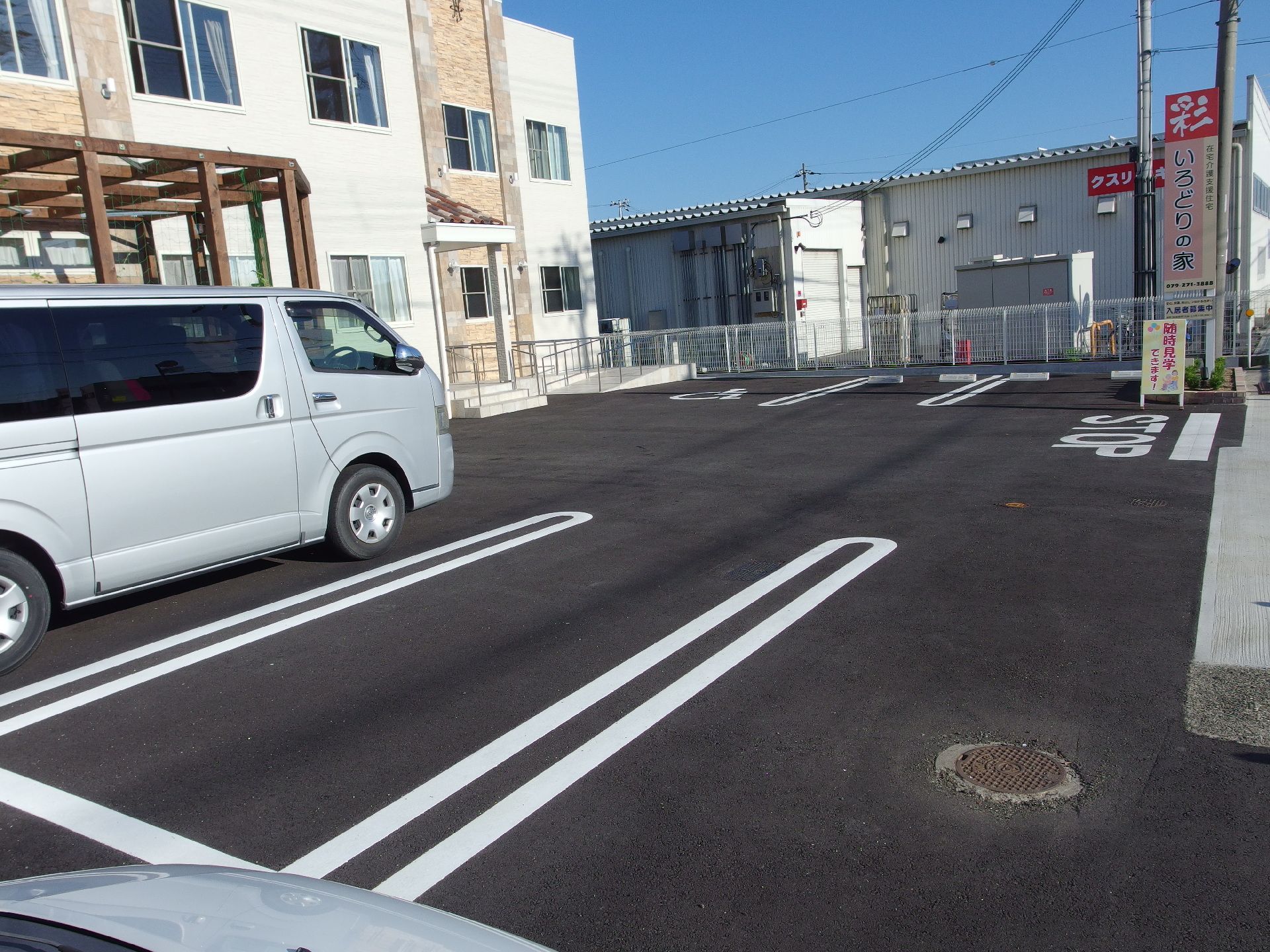 広々とした駐車場スペースに２台の白い車が駐車している。左奥には身体障害者用の駐車スペースがある。
