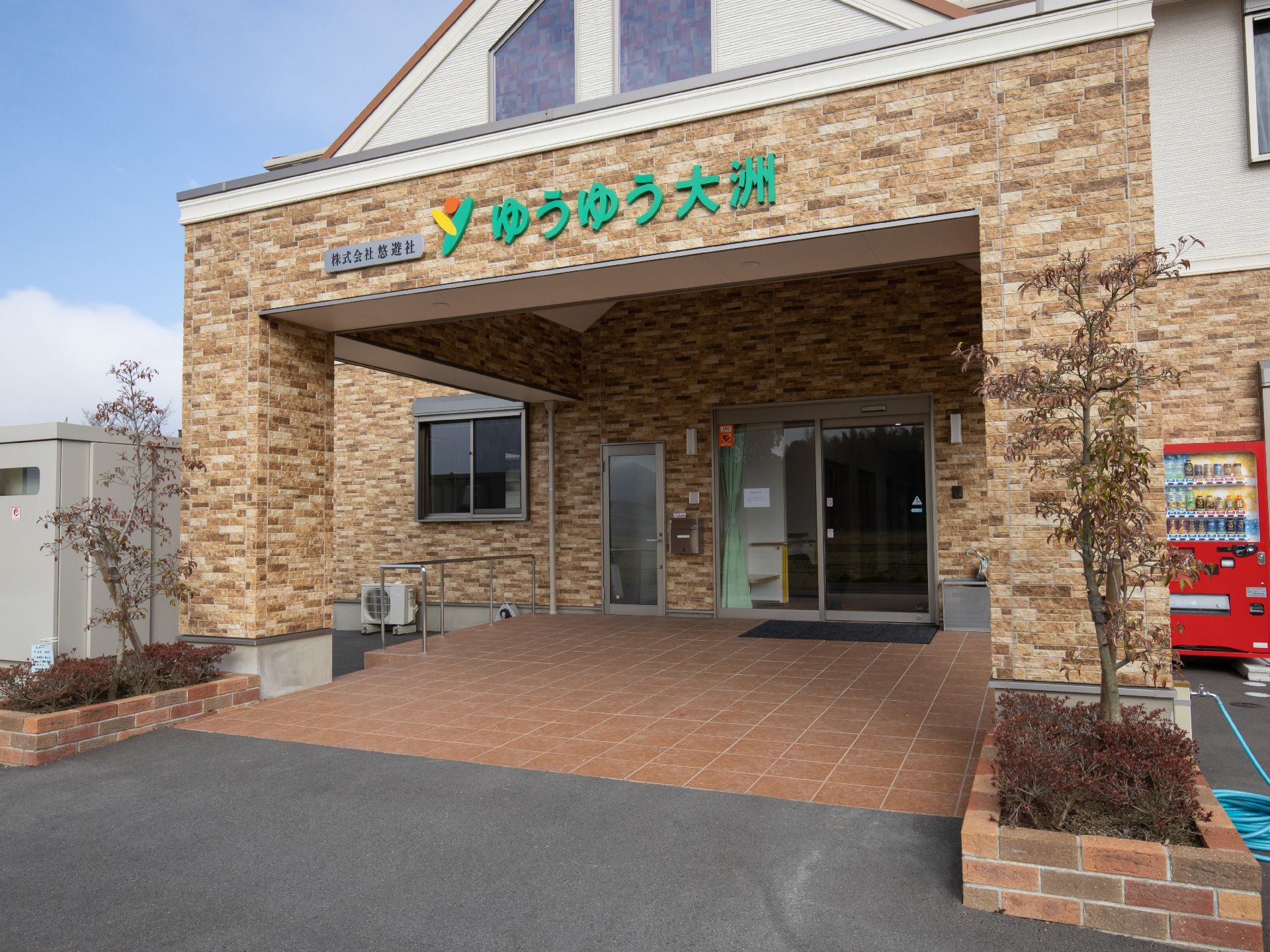 レンガ調の壁面になった建物で、玄関の上には三角の屋根がついている。出入り口は自動ドアになっていて、下には黒いマットが敷かれている。