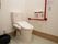 温水洗浄便座が設置されていて、壁には赤い手すりやトイレットペーパーホルダー、呼び出しボタンが取りつけられている。