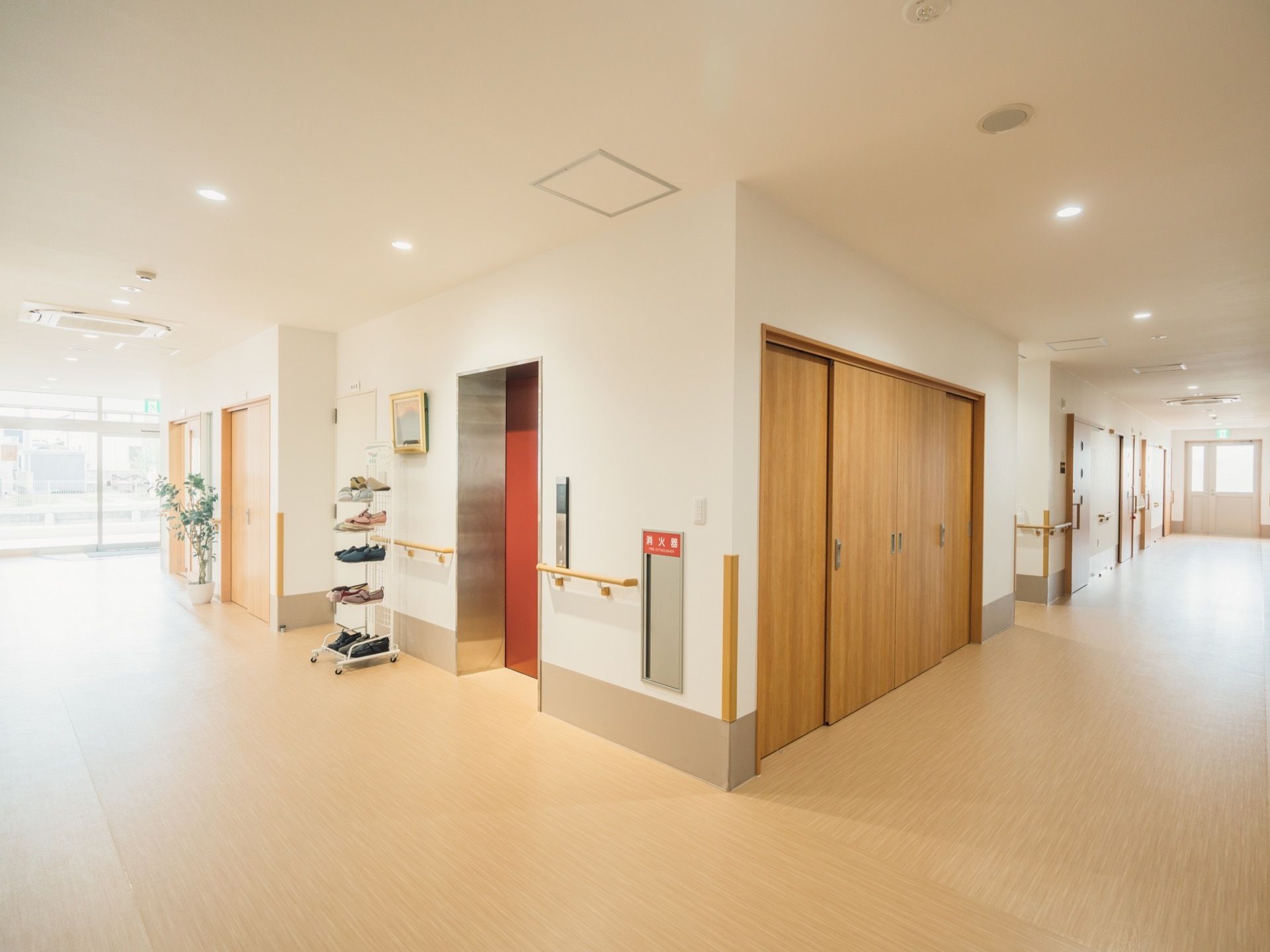 玄関から続く、手すり付きの広い通路があり。そのコーナー付近に、赤い扉のエレベーターが備えつけられている。