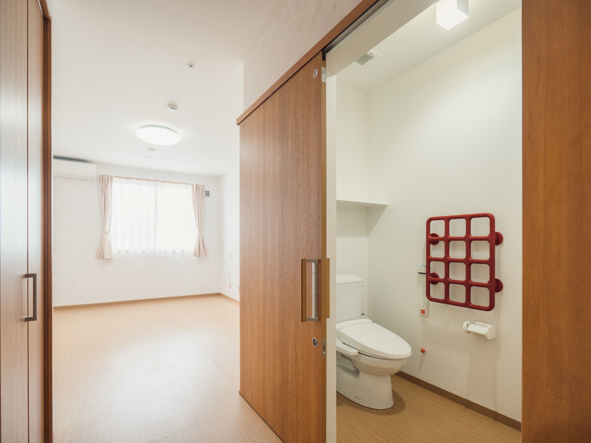 壁に赤色をした格子状の手すりが設置されているトイレ個室