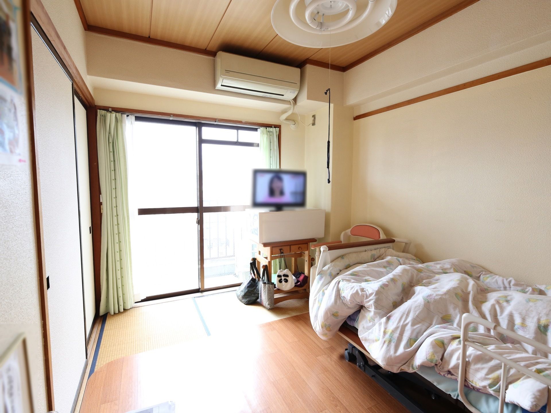 居室は、畳の上にフローリング模様のビニール素材が敷かれ、その上にベッドが置かれている。掃き出し窓がある。