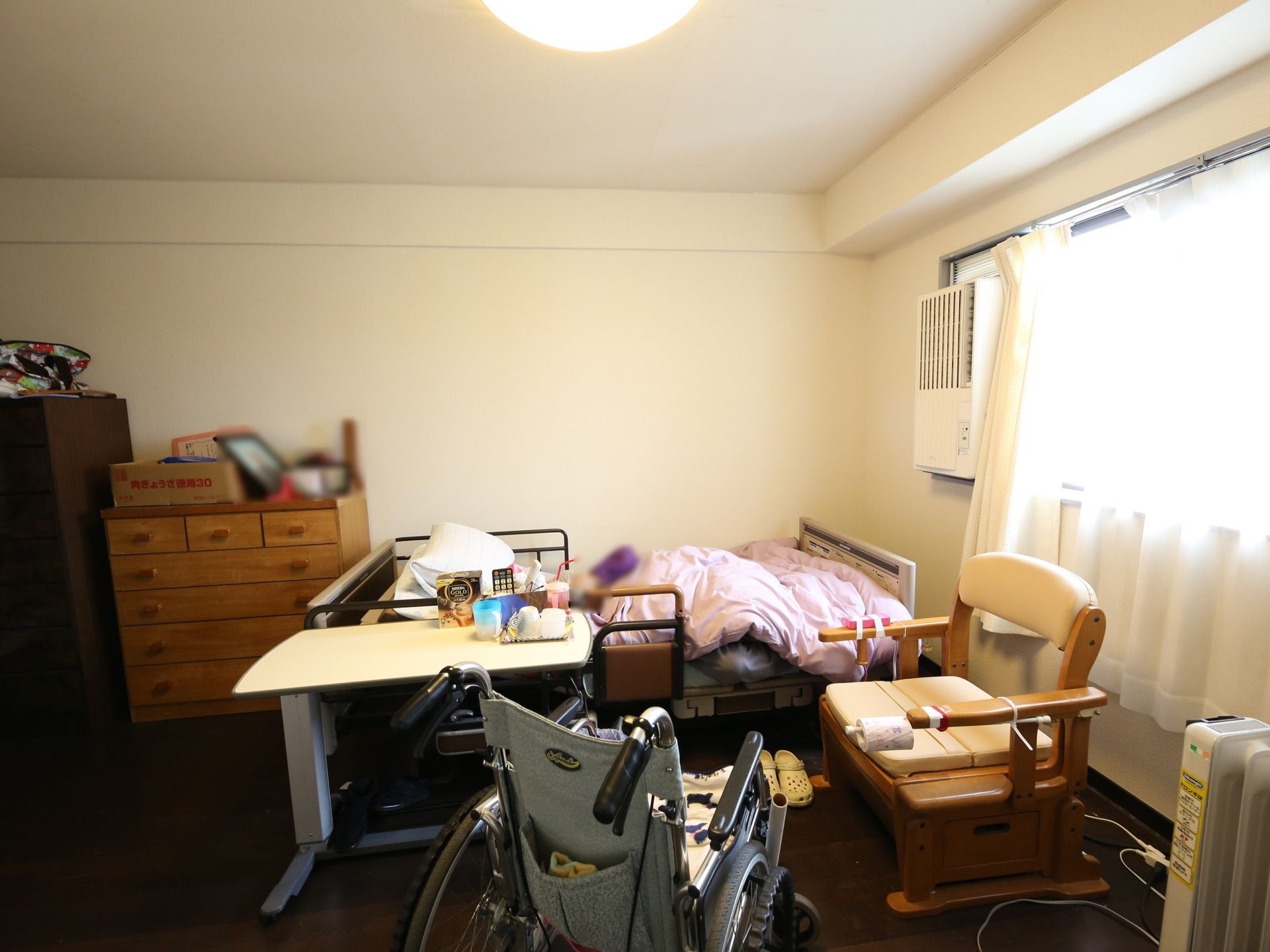居室の窓の近くに、転落防止柵つきの介護ベッドが設置されている。ベッドの横に、車椅子や室内用の椅子がある。