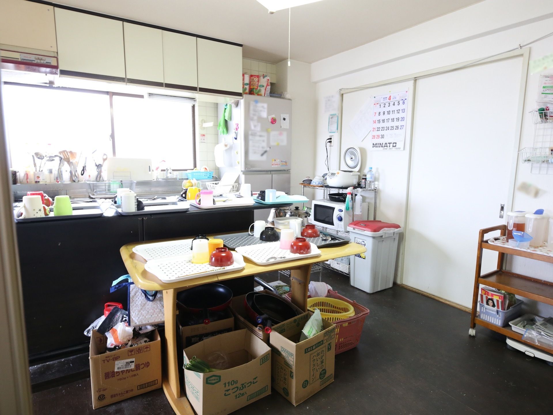 キッチンに、配膳用のトレイが並べられている。炊飯器や電子レンジ、大型冷蔵庫などが置かれている。窓際で調理器具が乾かされている。