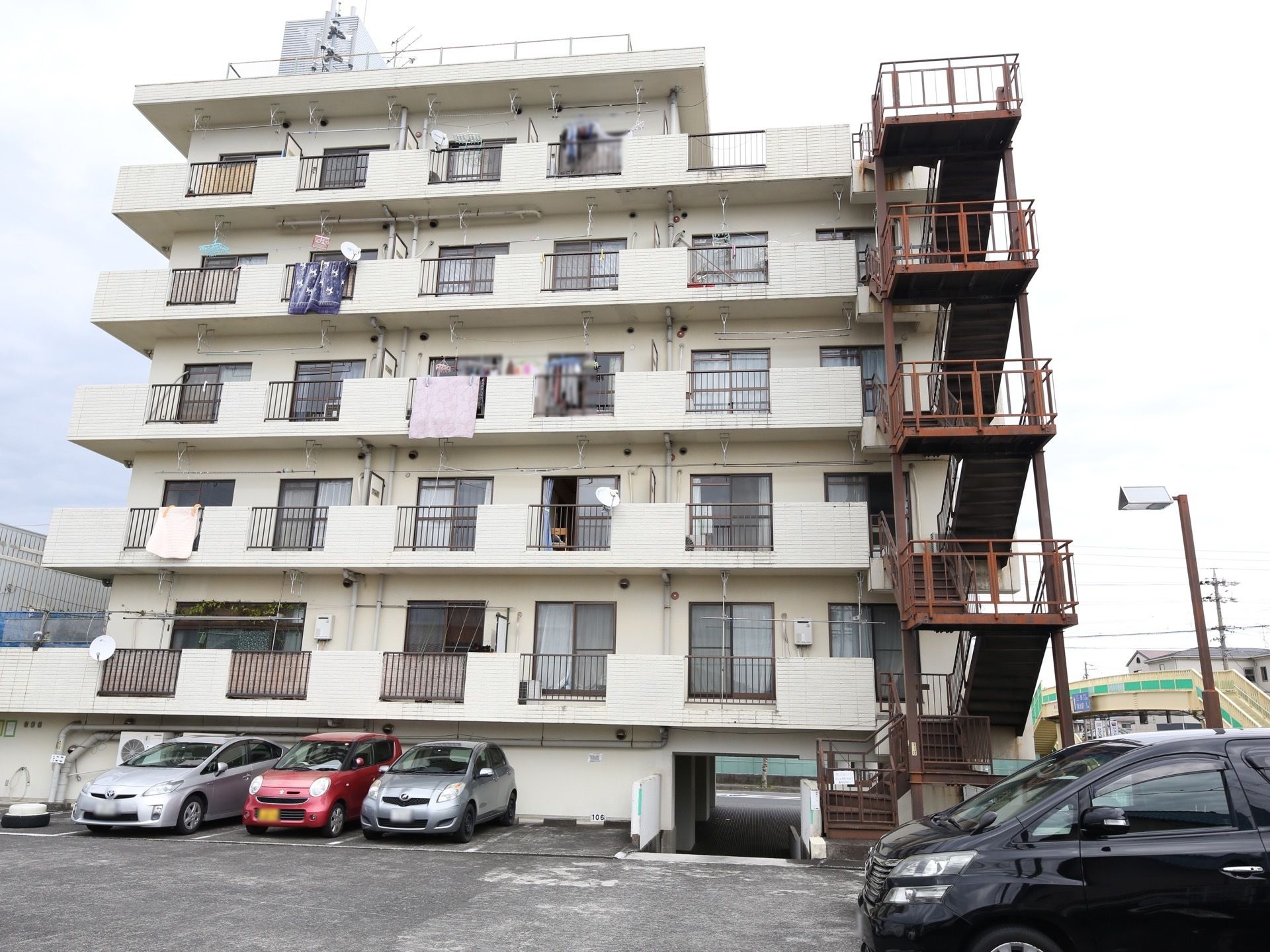 白色を基調とした６階建ての施設である。高さのある柵がついた茶色の避難階段が建物の横に設置されている。