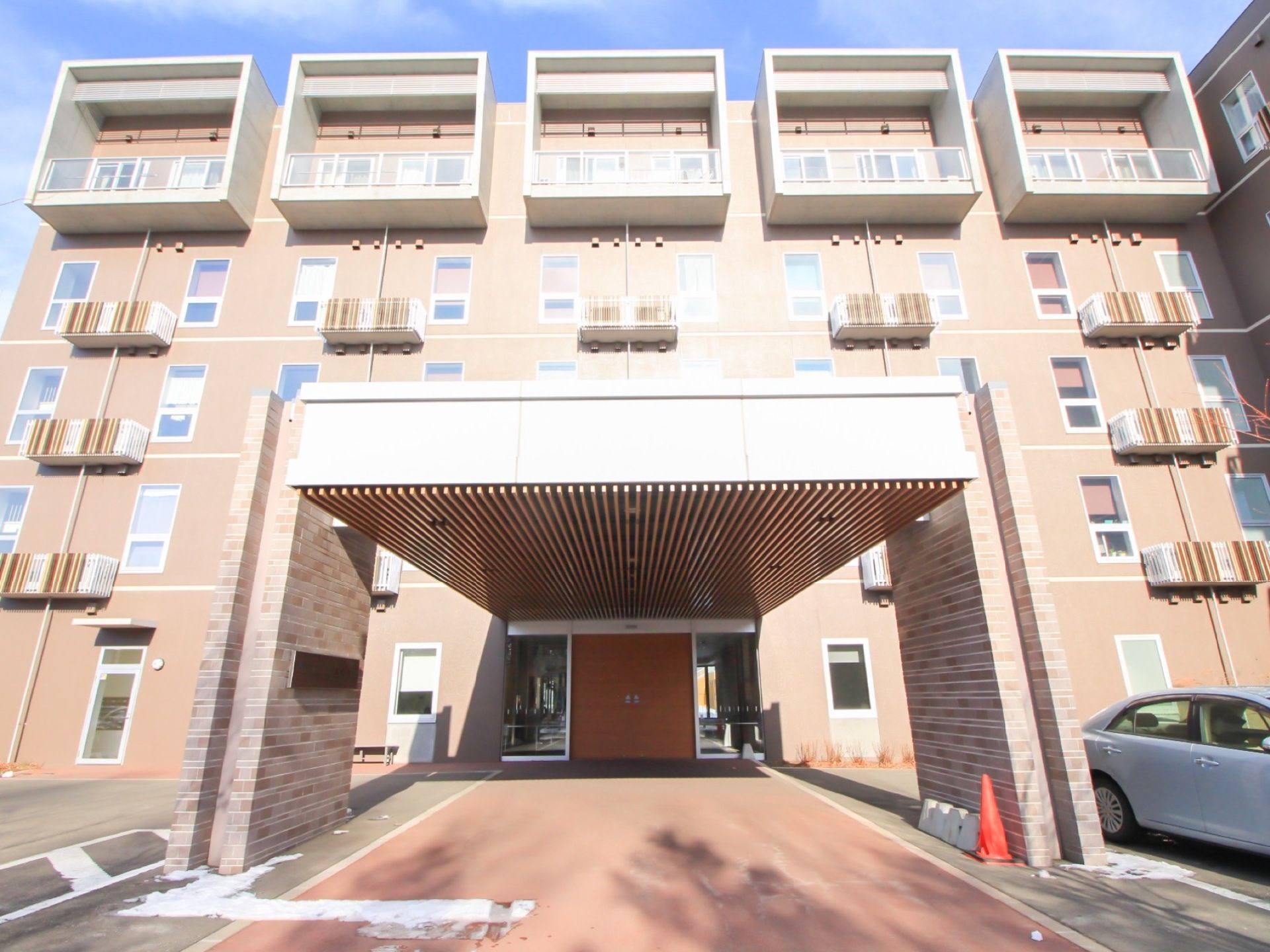 ５階建ての大きな重厚感のある住宅である。施設入口は屋根付きの車寄せが設けられており、近くには車が停められている。