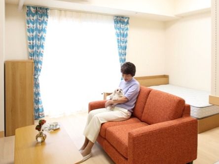 膝に小型犬を抱えた女性が赤いソファーに座っている、居室の様子。
