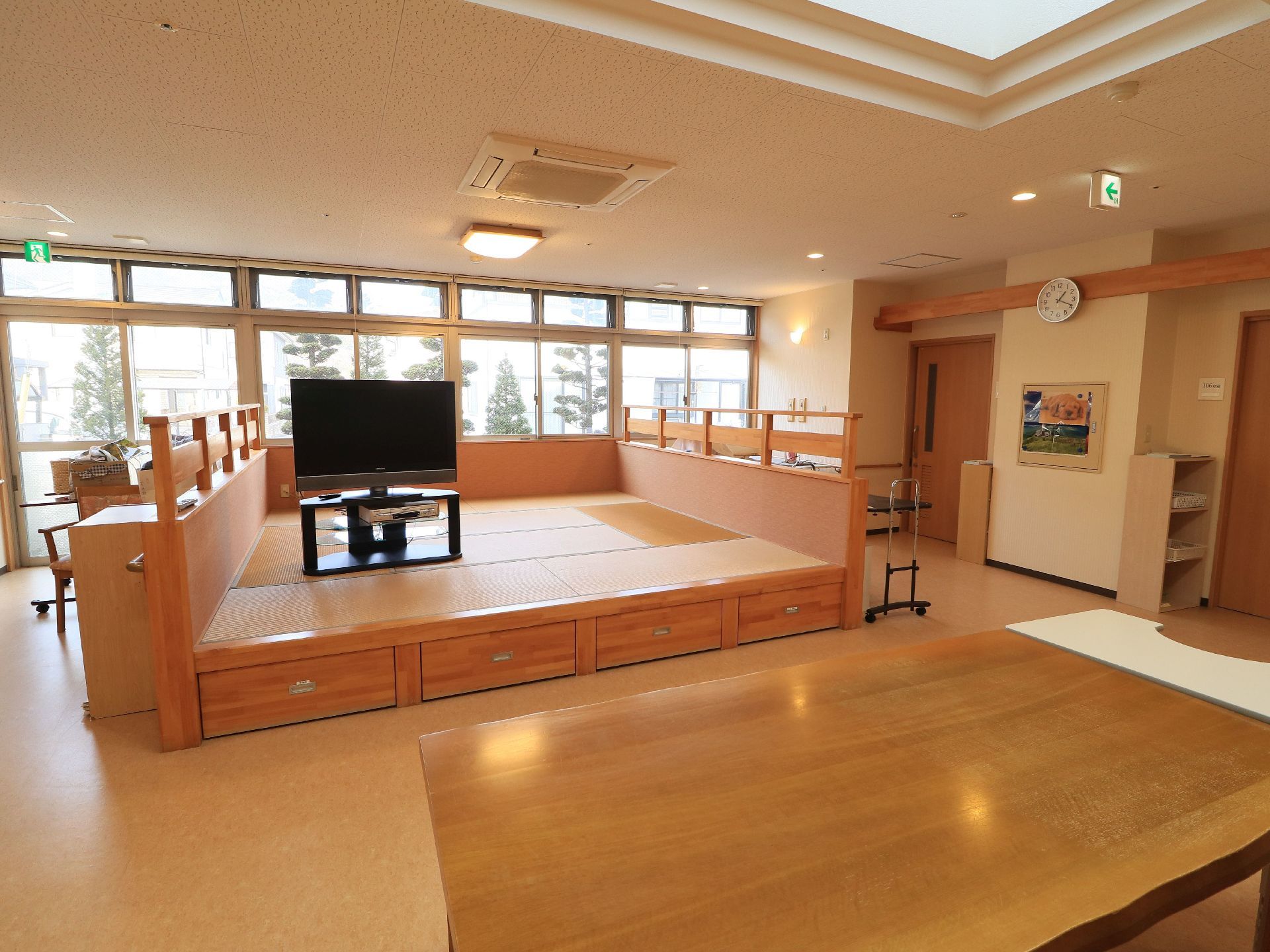 広々とした集会室には畳コーナーが設けられており、テーブルやカラーボックスが置かれている。奥には、庭が見える窓がある。
