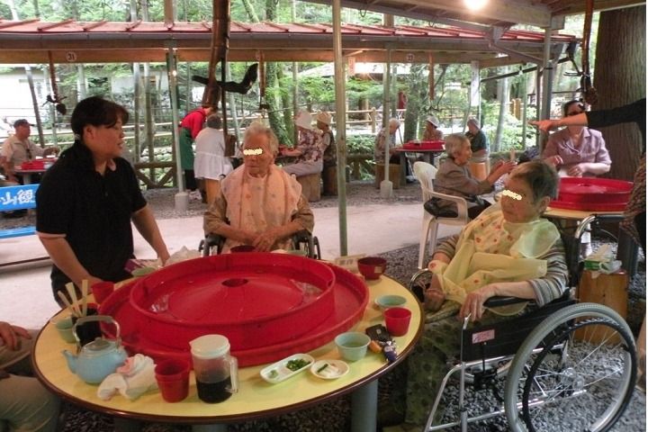 屋外でそうめん流しを楽しむ車いすの入居者とスタッフ。そうめんが回っていた入れ物はほぼ空。