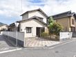 通りの角地に面して建っている。白い外壁の２階建ての建物で、玄関前に植栽が植えられている。床は３色のブロックが敷かれている。