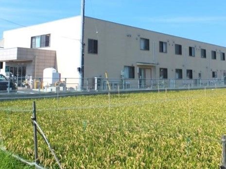 ２階建ての建物が写っている写真。目の前に広めの畑らしきものが写っている