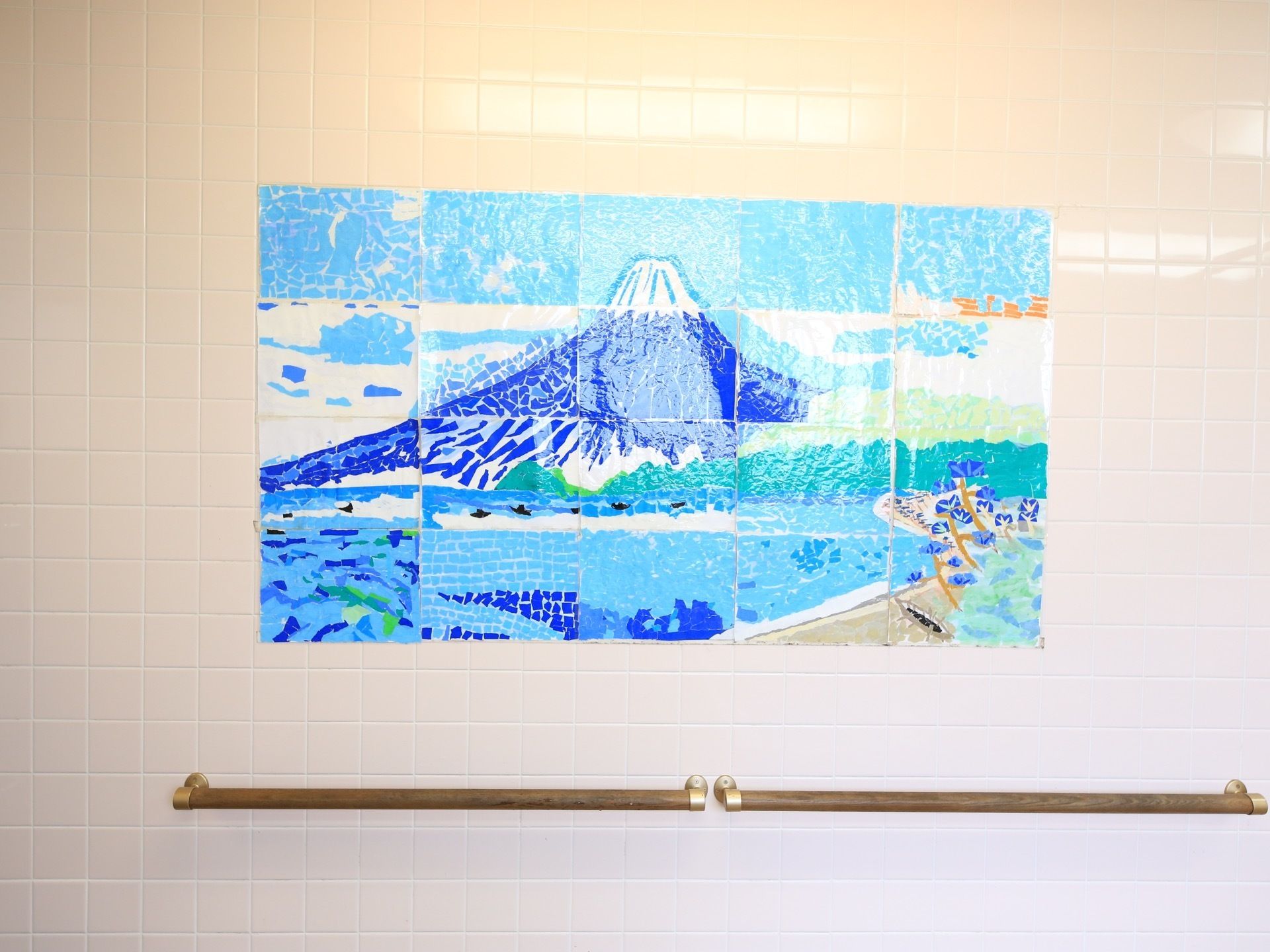 浴室の洗い場付近の壁タイルに描かれた海と山の絵である。絵の下には、横に２本の手すりがある。