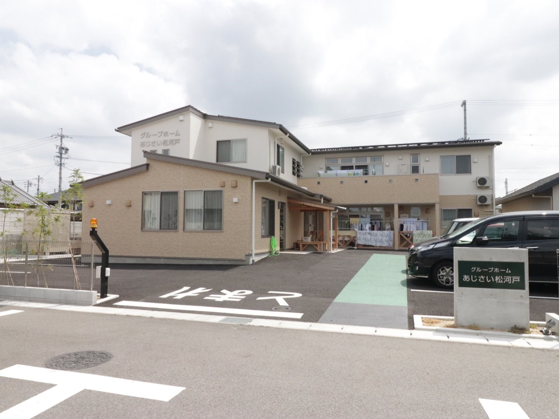 駐車場の奧にＬ字型の２階建ての施設が建っている。建物の２階の壁面や、駐車場入り口付近に施設名称が明示され、わかりやすい。