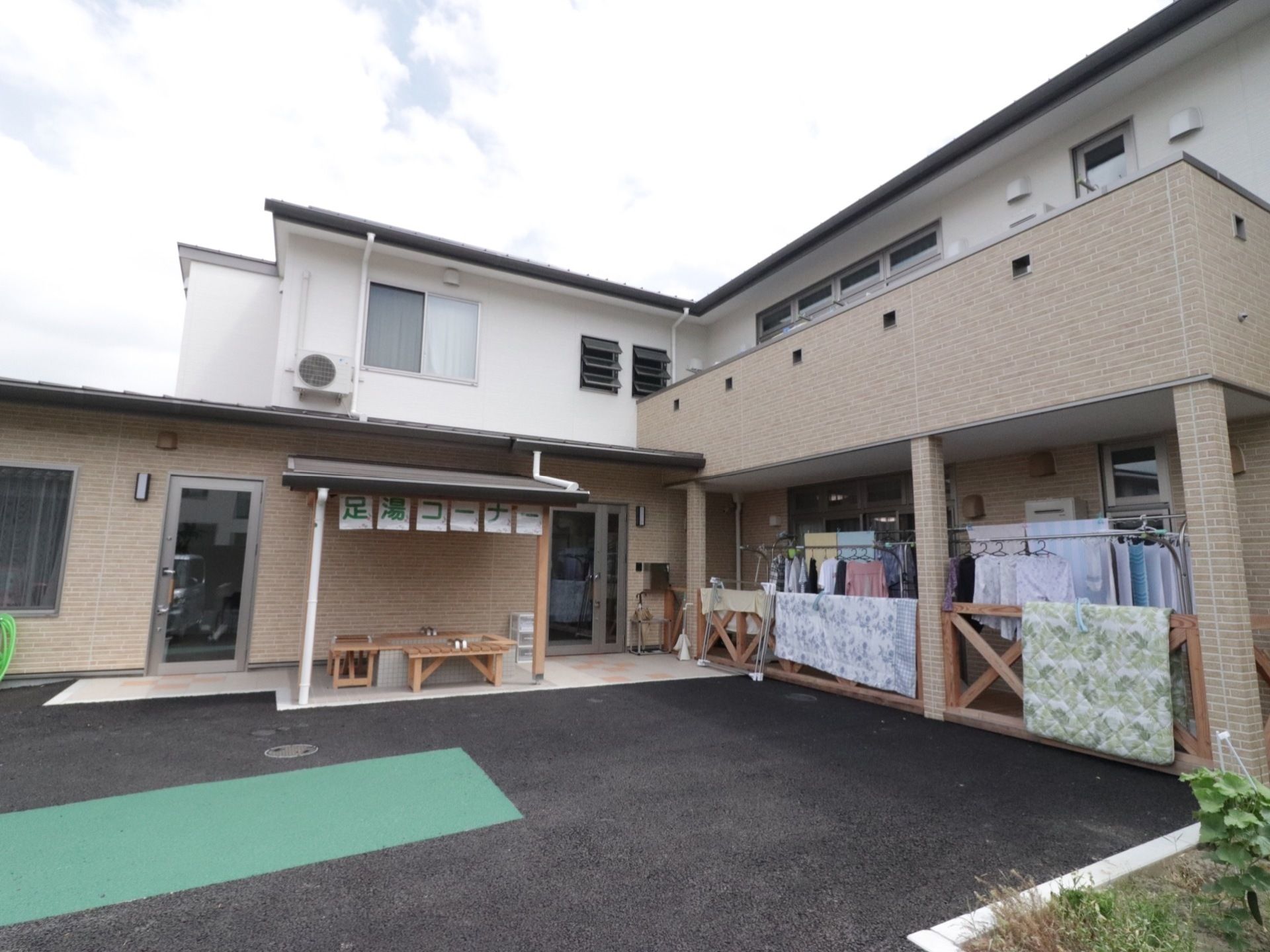 Ｌ字型の２階建ての施設の前に足湯とベンチが設置されている。テラスには洗濯物がたくさん干されているのが見える。