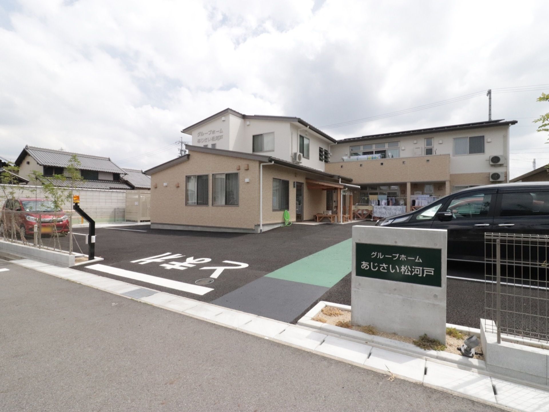 ホームのイメージ。2階建ての建物の周辺医は車いすの人や杖を突く高齢者が。建物の前には駐車スペースもある。