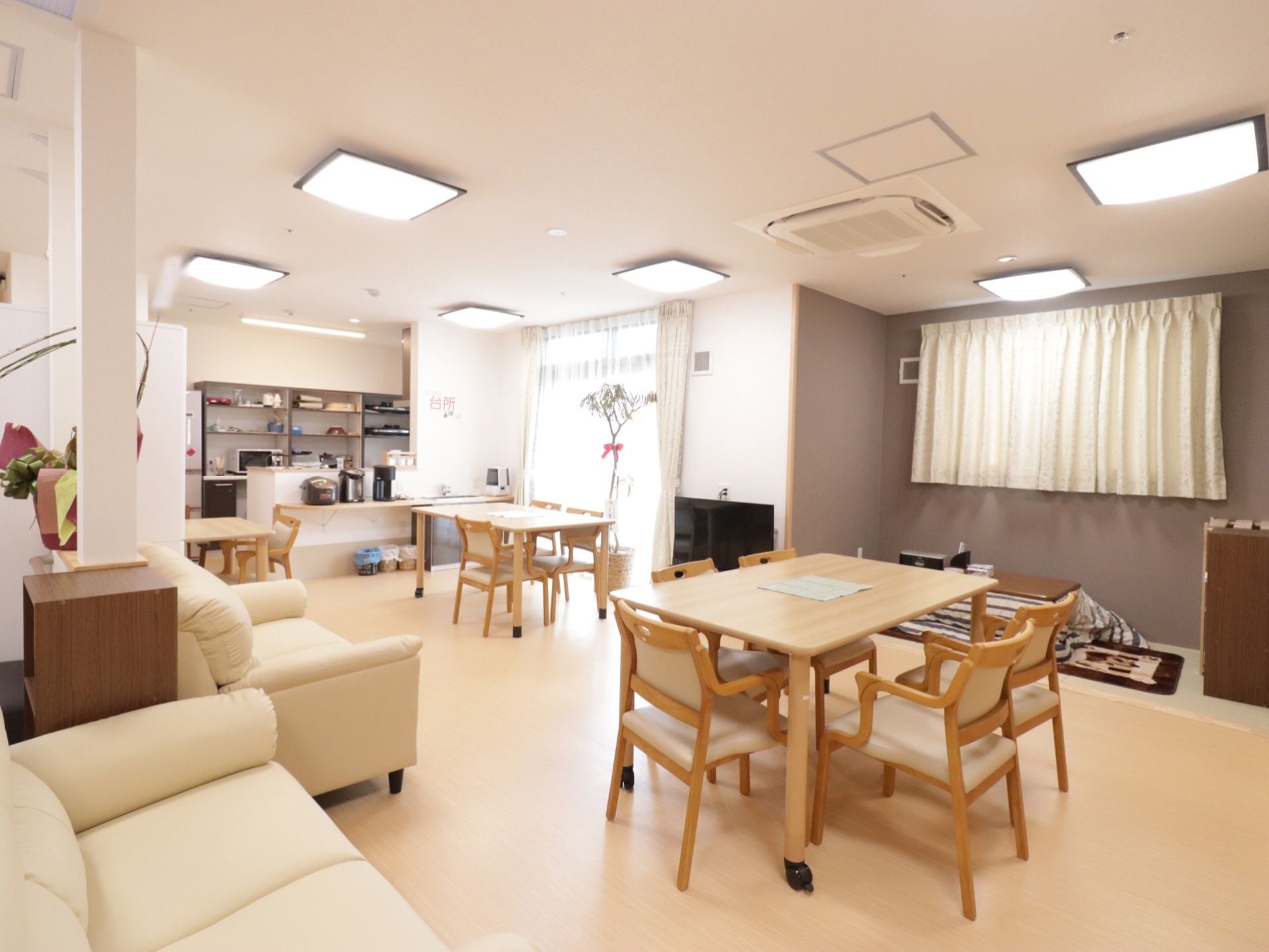 ソファやダイニングテーブルが並んだ広い空間がある。奥の床にはコタツが置かれている。カウンターには炊飯器やポットが並んでいる。