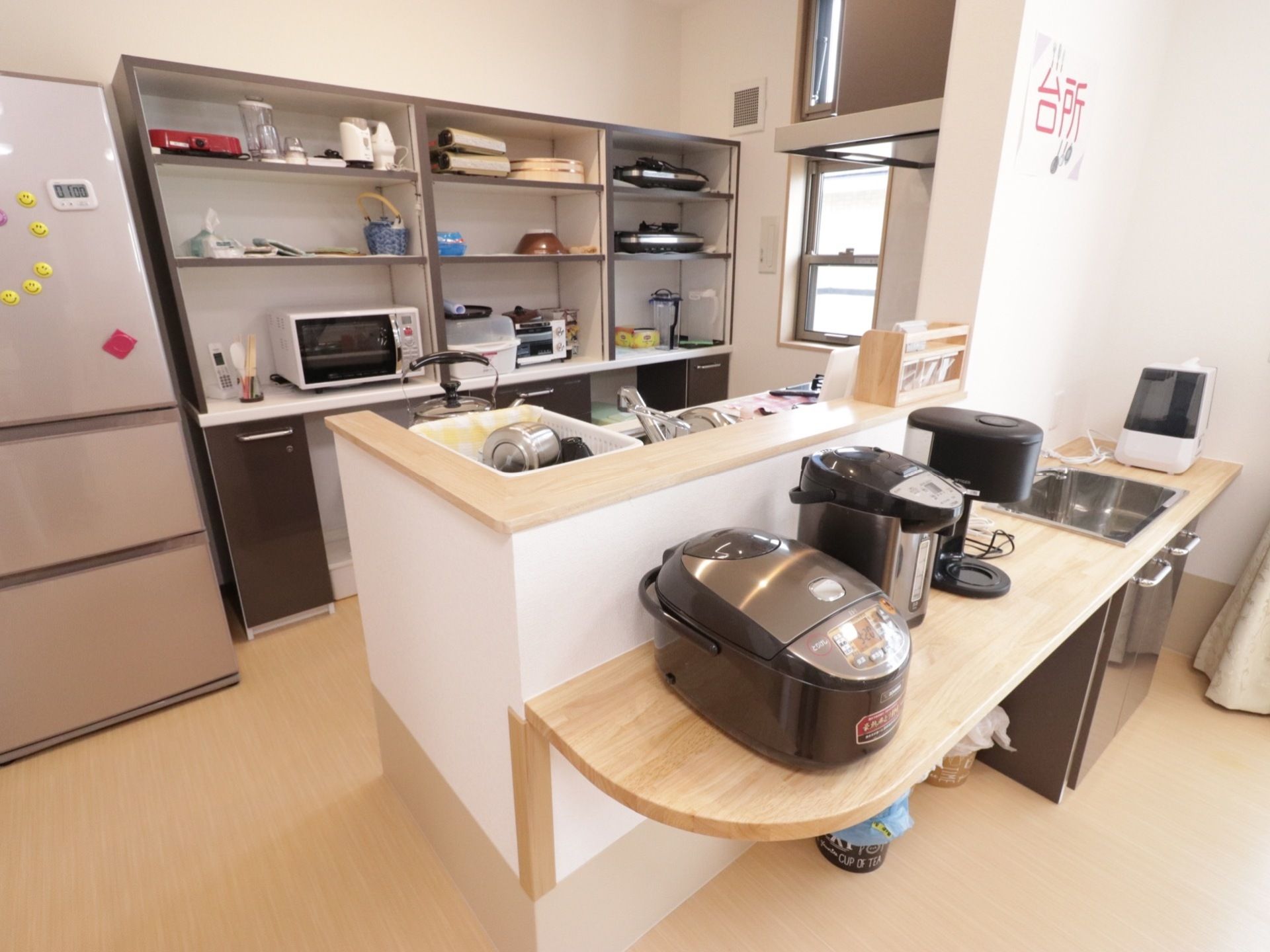 キッチン前のカウンターには炊飯器やポットが並んでいる。奥の食器棚には食器の他、調理器具が収納されている。