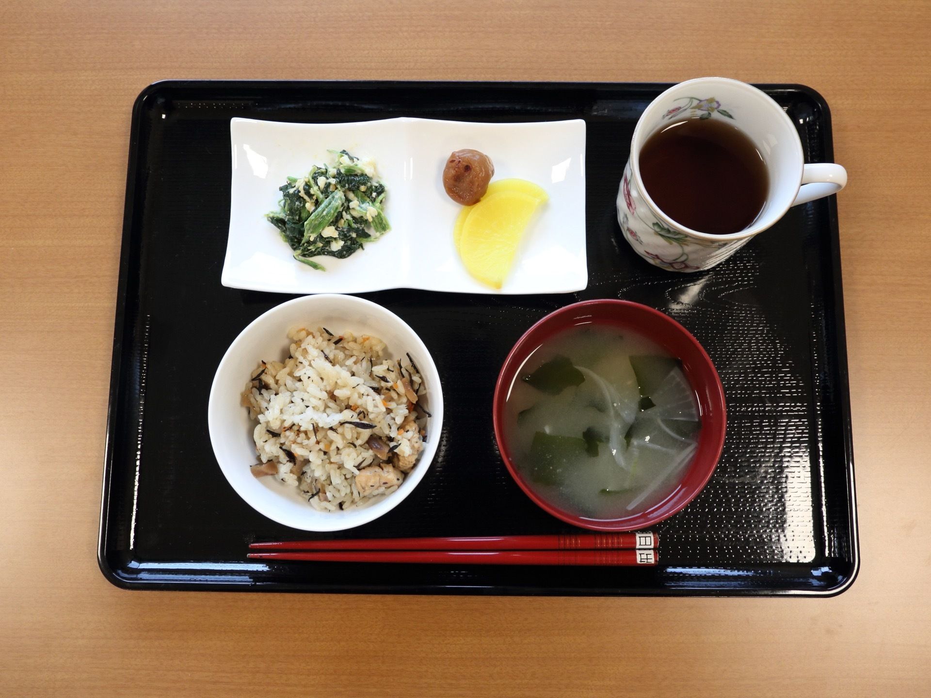 黒塗りの盆に、ごはん、汁物、おかず、お茶がセットされている。食事はさまざまな食材を使用して、栄養バランスの取れたメニューが提供されている。