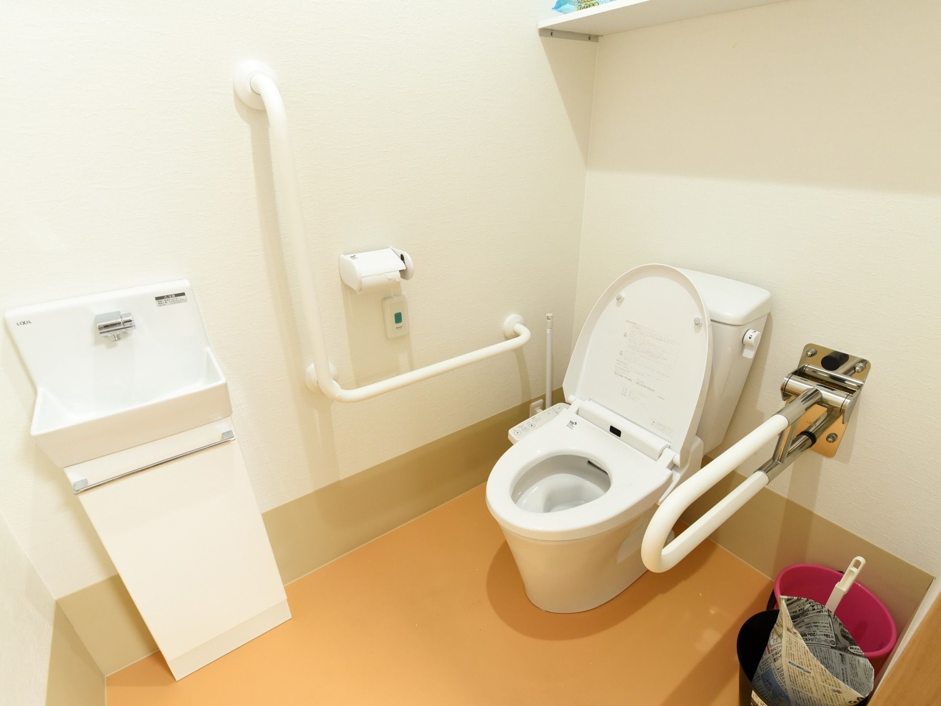 白い壁の明るいトイレ。便器の両側に手すりを設置しており、立ち上がる際に体を支えることができ安全である。