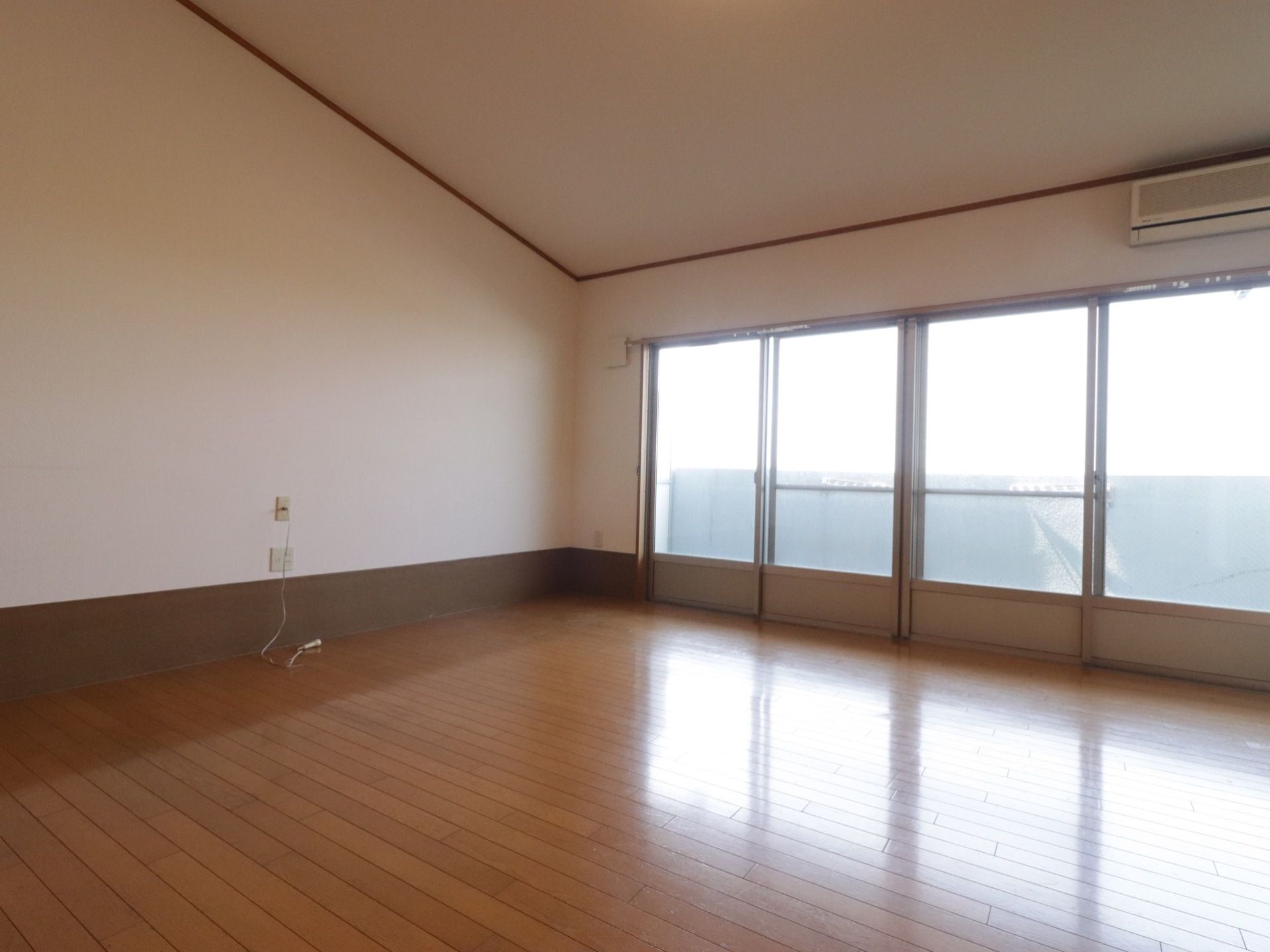 フローリングの広々とした居室には大きな掃き出し窓があり、明るい日の光が入る。壁にはエアコンやヘルプコールが備わっている。