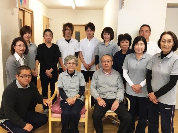 高齢者夫婦を囲んで微笑むスタッフの様子。施設内の写真