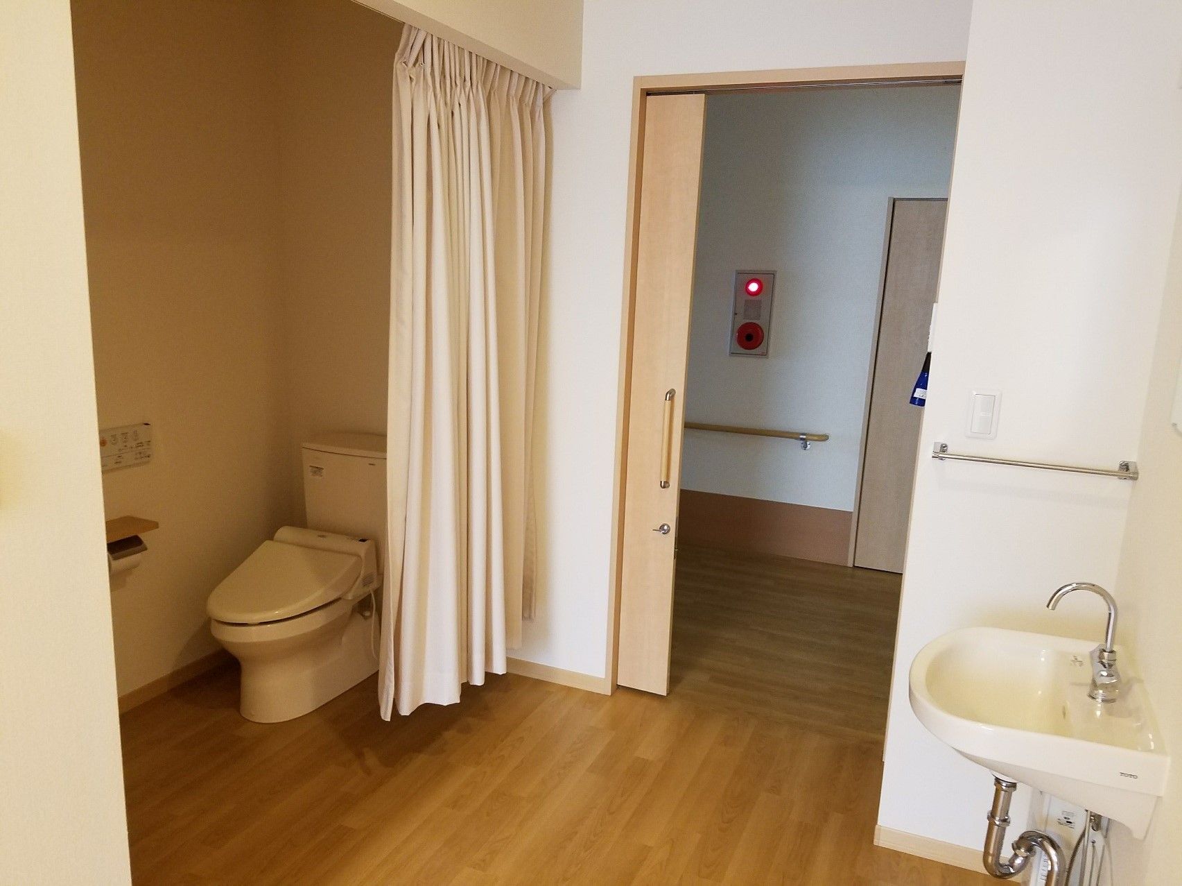 カーテン式のトイレがある個室。洗面台が手間に移っている様子が分かる