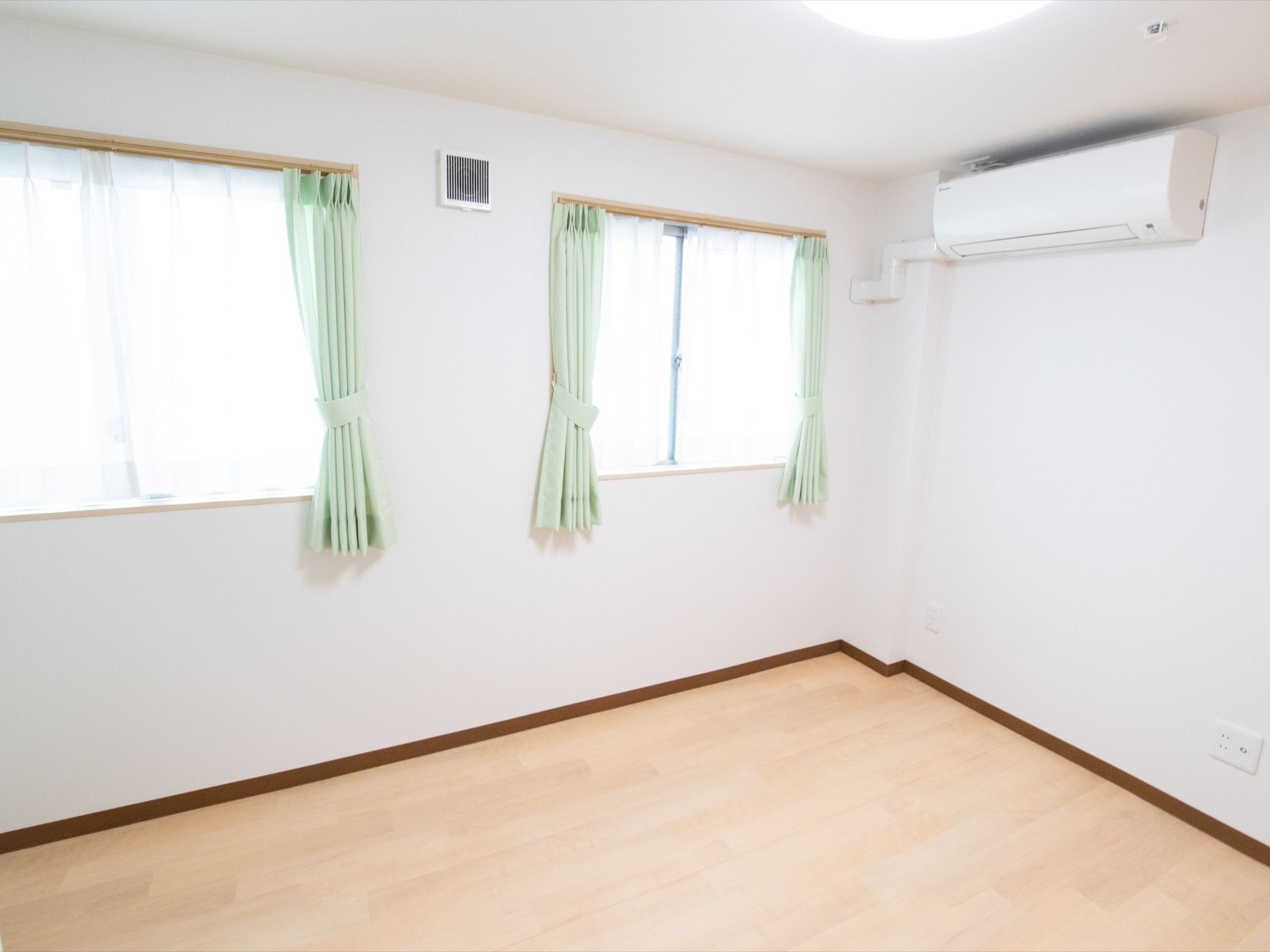 居室の側面には窓が並んでいる。壁の下側にコンセントを設置し、テレビも備えることができる。お部屋の角の上部にエアコンを取つけている。