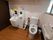 木目調のフローリングの広々としたトイレスペースである。便座の両側に手すりを完備し、隣に深さのある洗面台を設けている。
